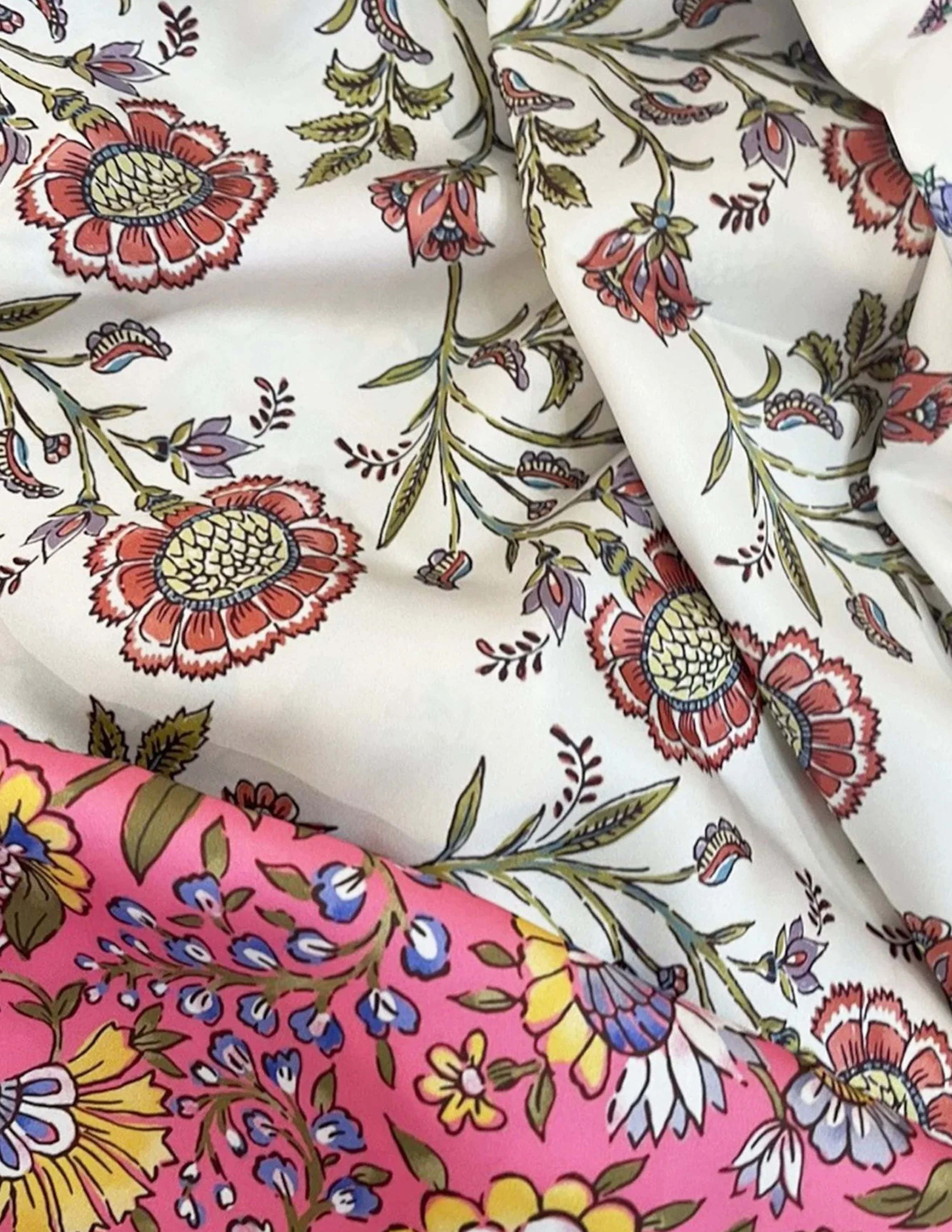 Close-up image of floral patterned fabric with large, detailed flowers and leaves in red, purple, yellow, blue, and green on a white background.