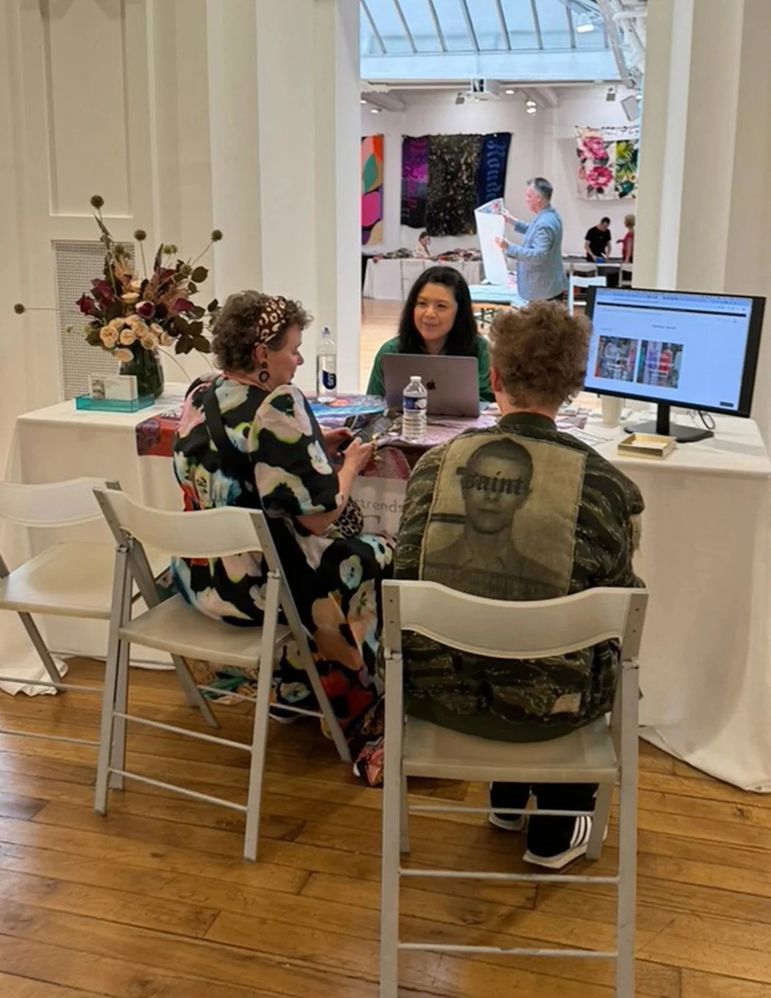 People sitting at a table engaging in conversation at an art gallery. There are colorful artworks hanging on the walls in the background.