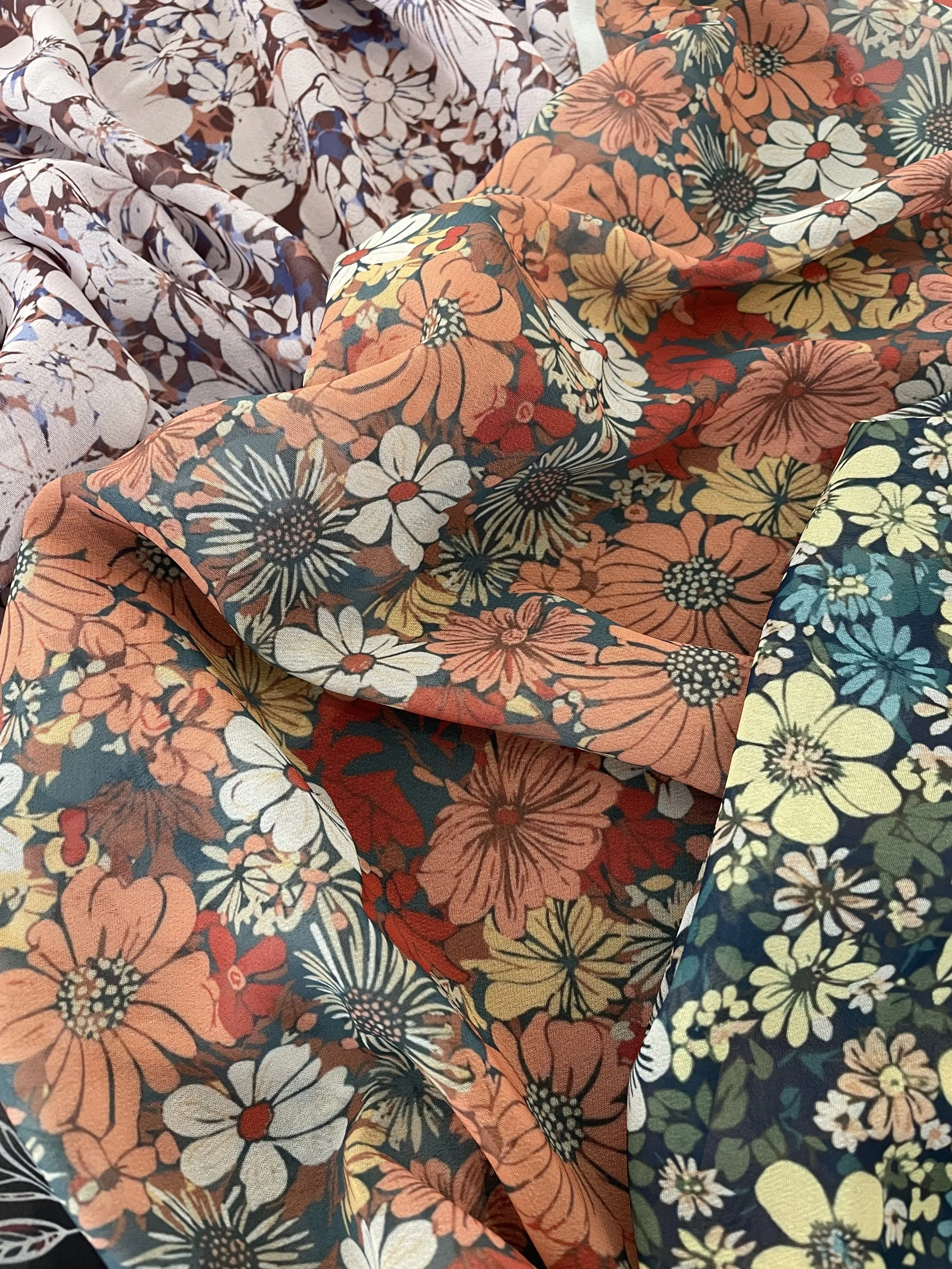 Close-up of colorful floral patterned fabrics with orange, white, yellow, and dark background designs.