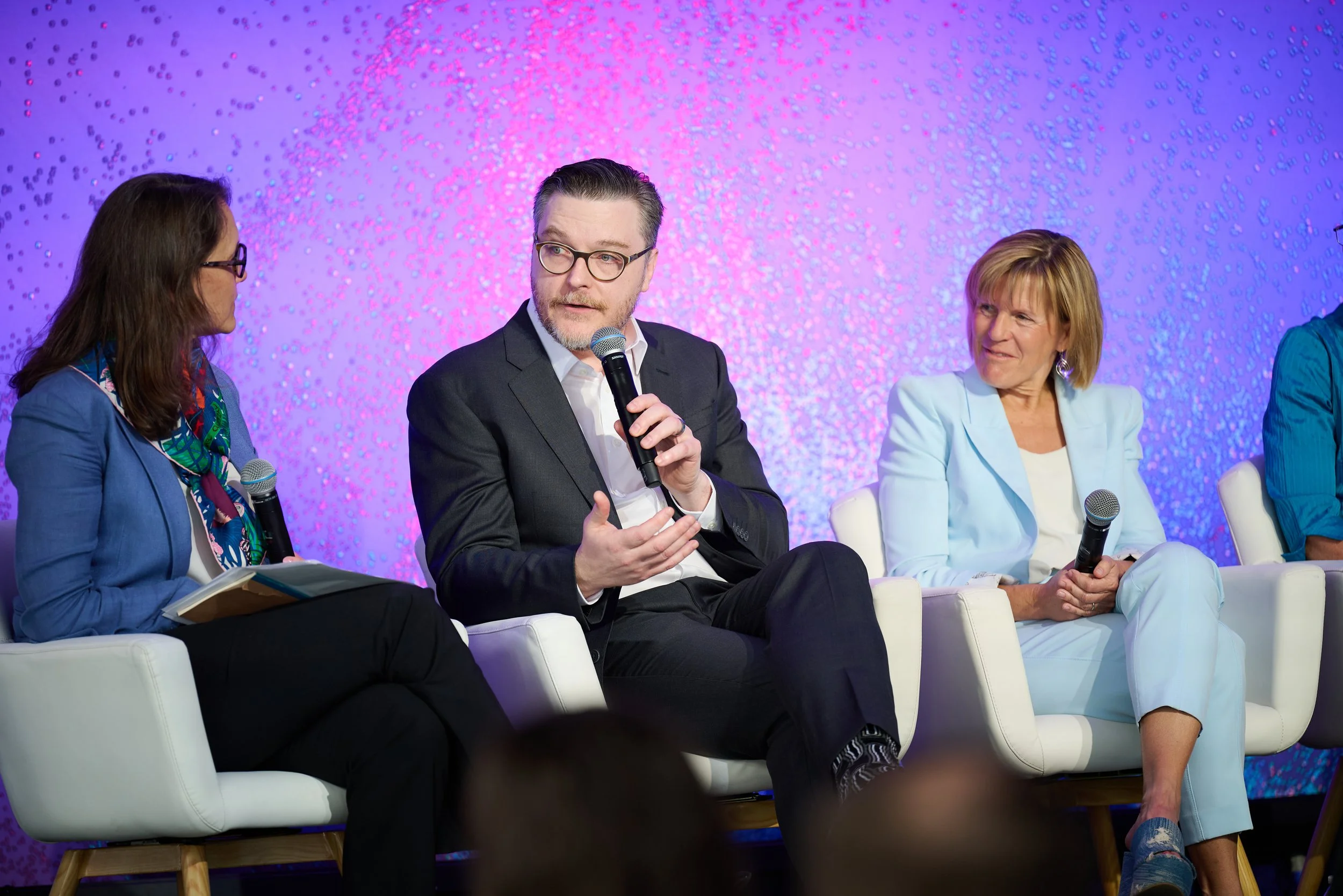 A panel discussion with people sitting on a stage, Tommy Bishop speaking into a microphone at the ASU+GSV Summit.