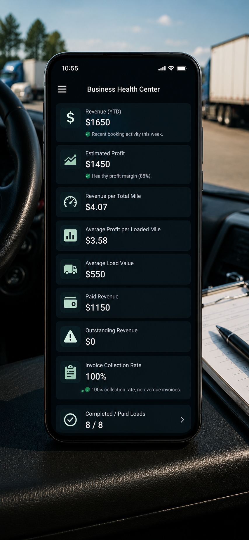 A smartphone displaying a business management app with financial data, sitting inside a vehicle with a clipboard and pen nearby, and trucks visible outside.
