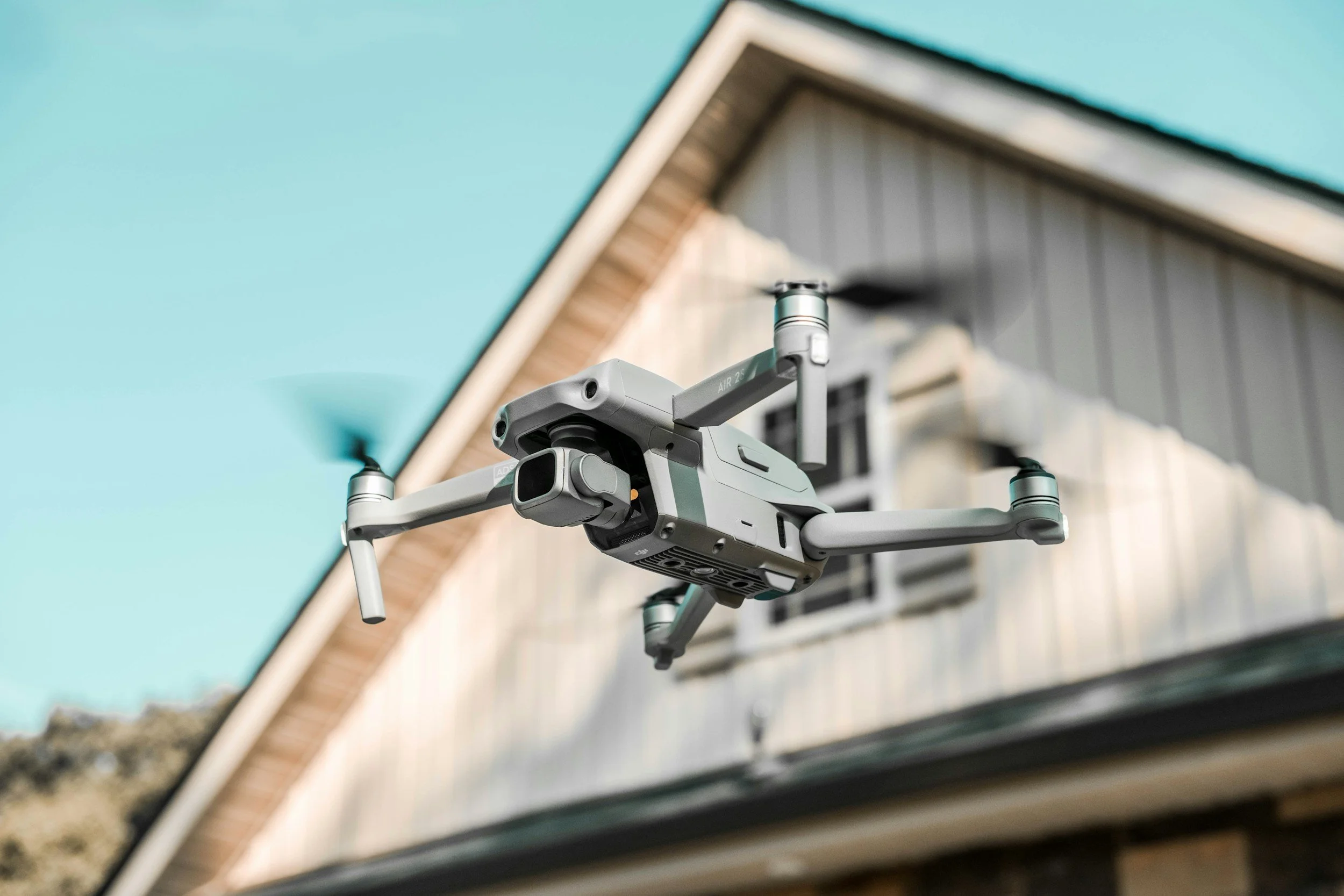 Eine Drohne fliegt vor einem Haus mit grünem Dach.