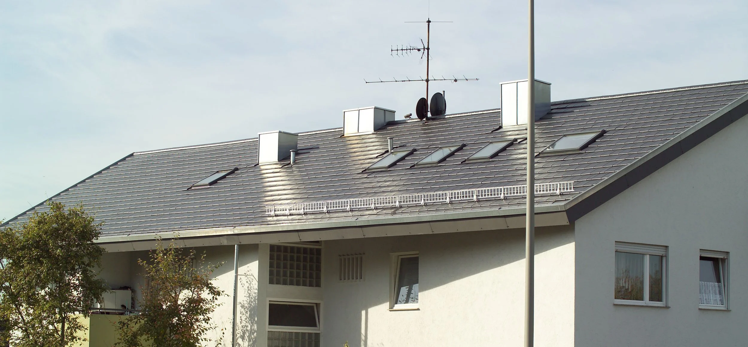Dach eines Hauses mit Dachfenstern, Antennen und einem Satellitenschüssel, nahem Baum