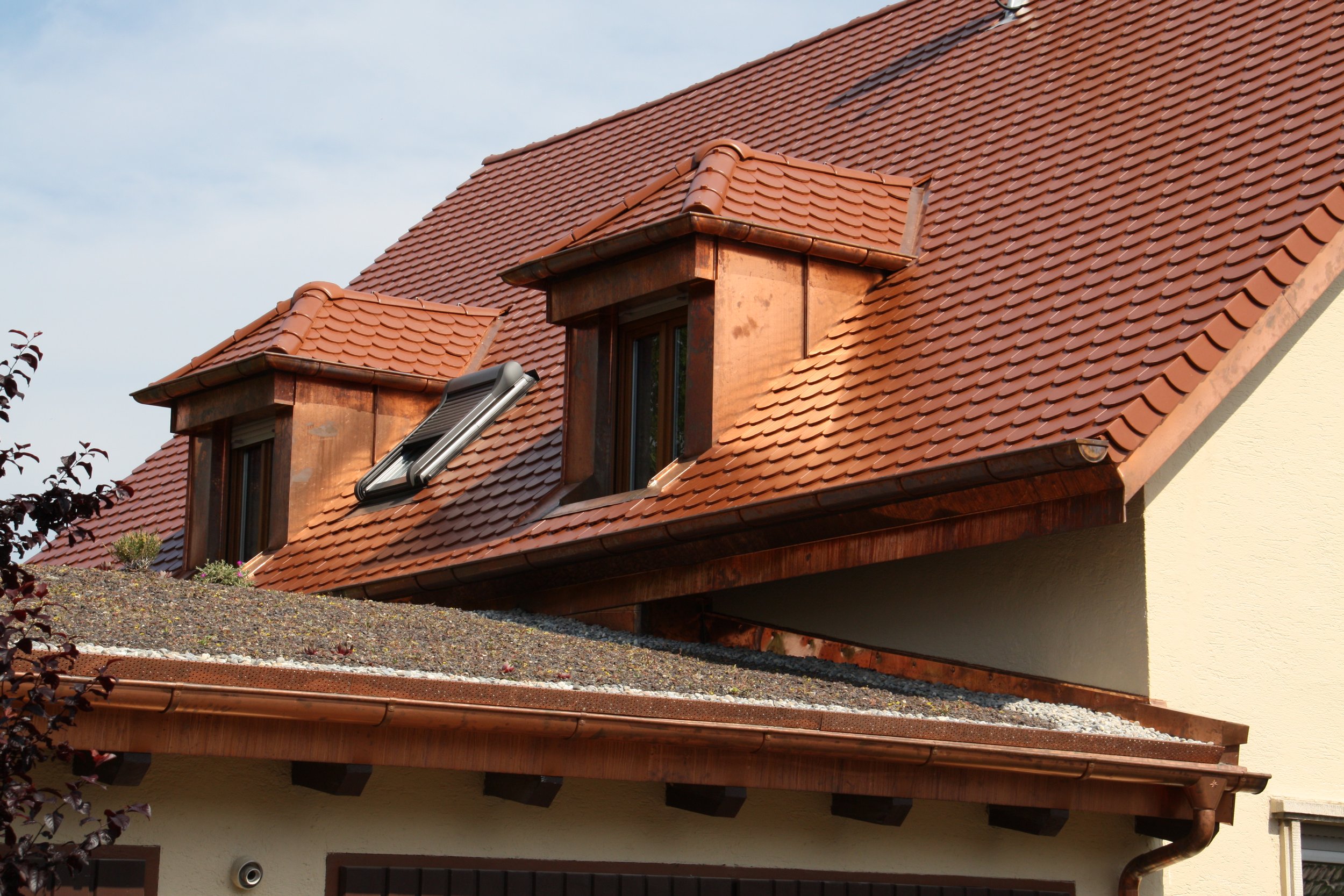 Dach mit roten Ziegeln, auf dem ein Solarpanel installiert ist. Das Haus hat Dachfenster und eine Dachrinne.