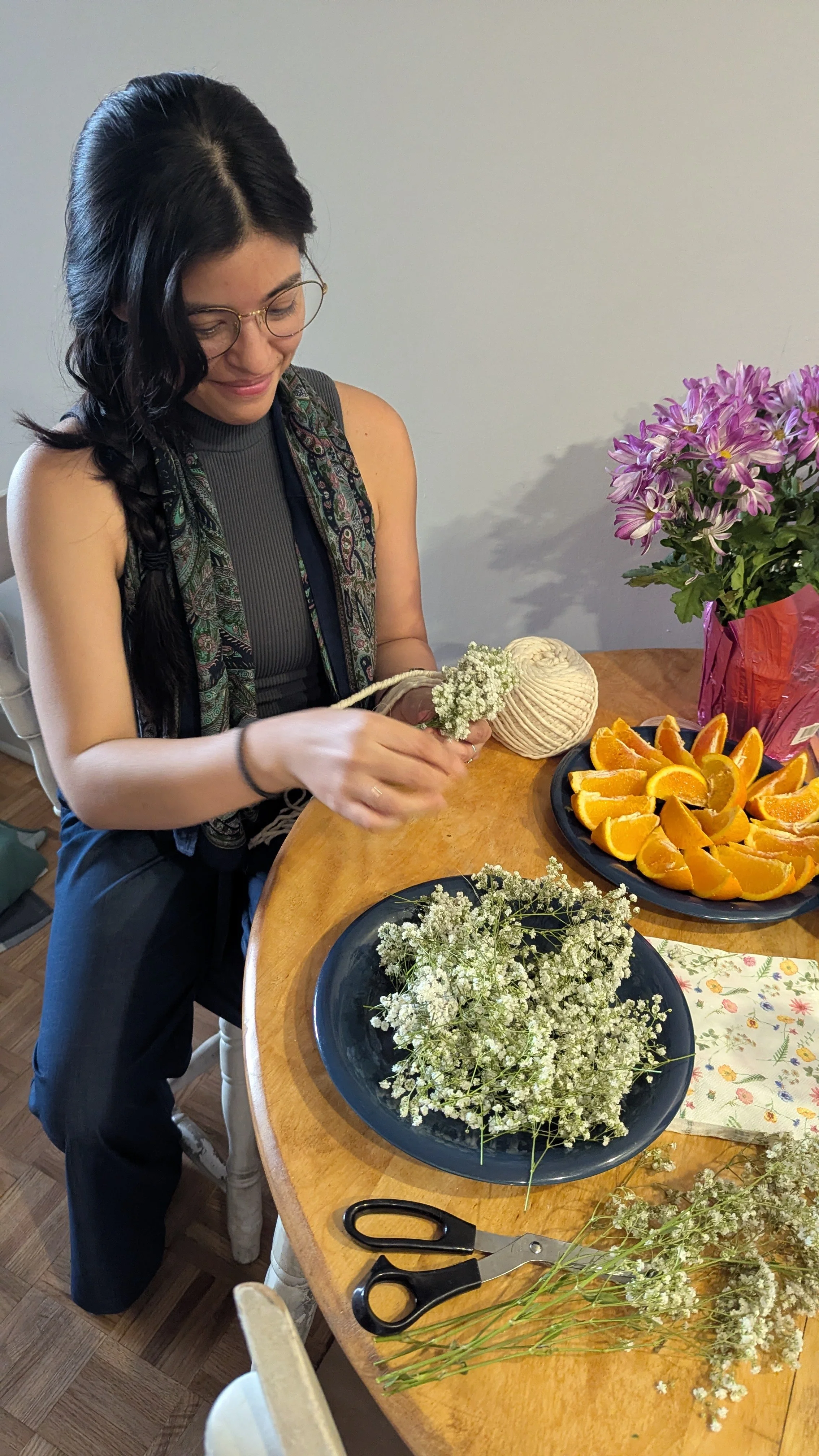 Ale la Doula smiling while tying small white flowers together at a table, representing her holistic approach to prenatal support.