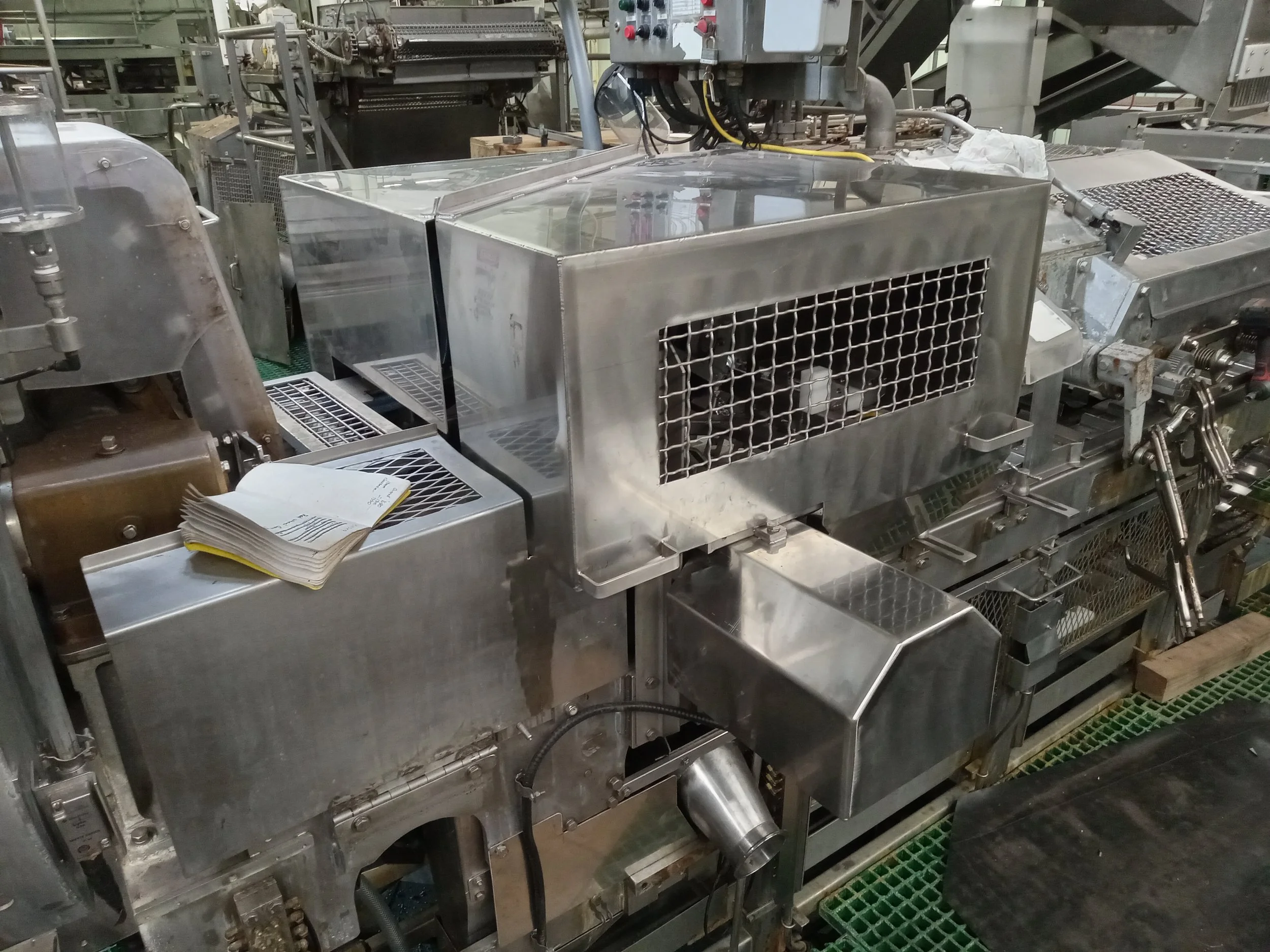 Industrial machinery made of stainless steel with various pipes, controls, and grills, likely used for manufacturing or processing in a factory setting.