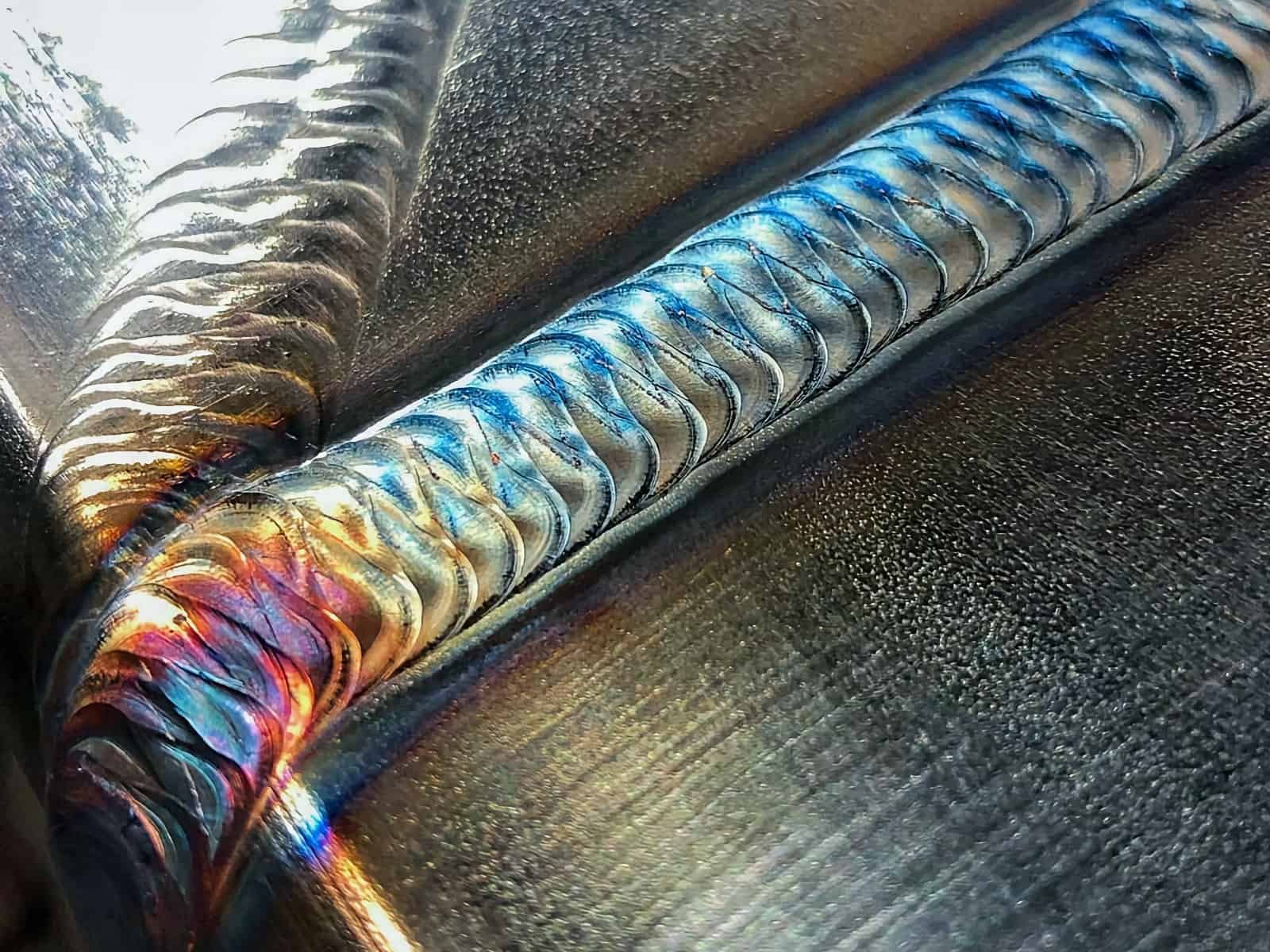Close-up of a welding process on metal, showing vibrant colors and sparks along a weld seam.