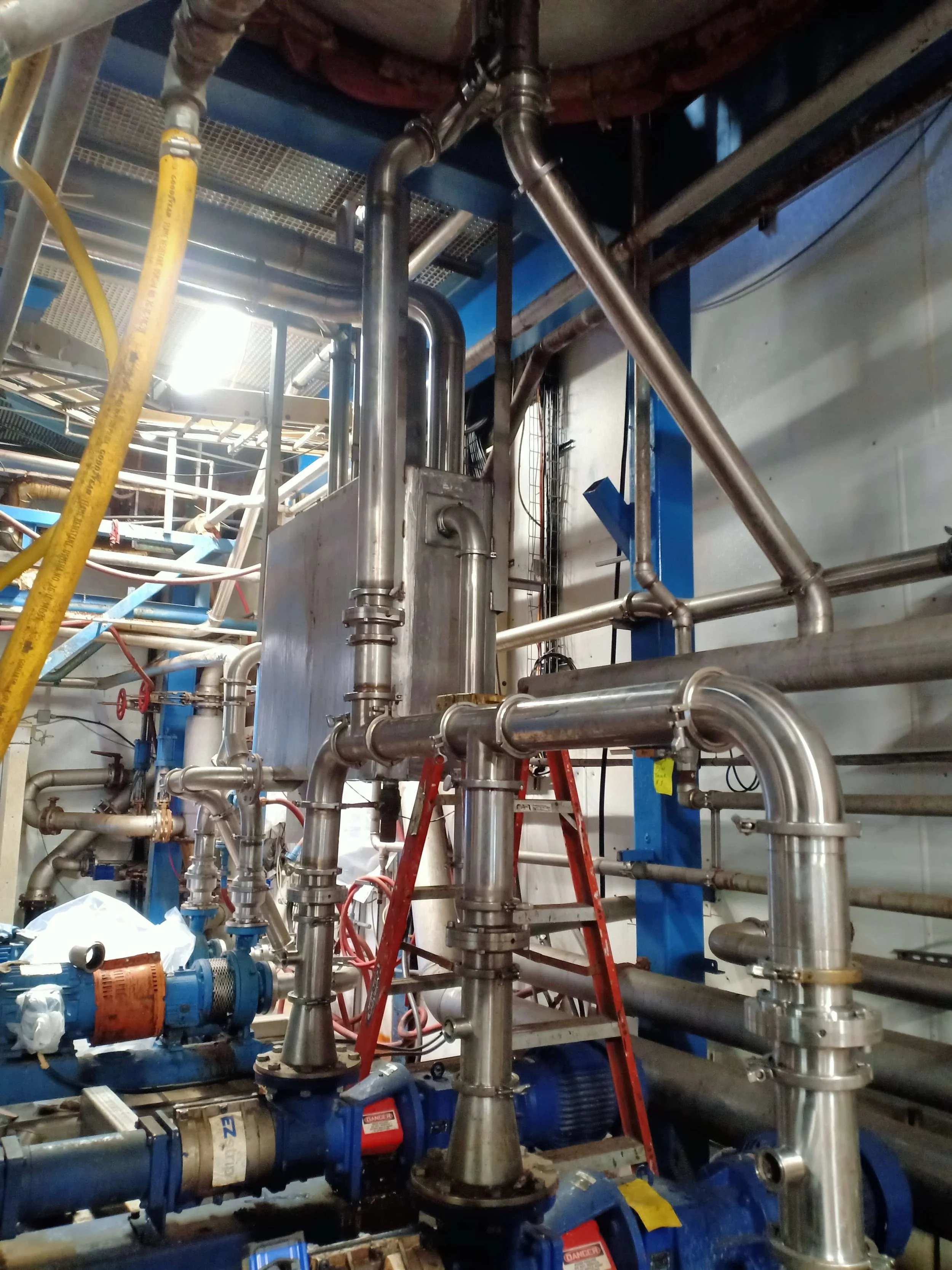 Industrial piping system with metal pipes, valves, and machinery in a factory setting.