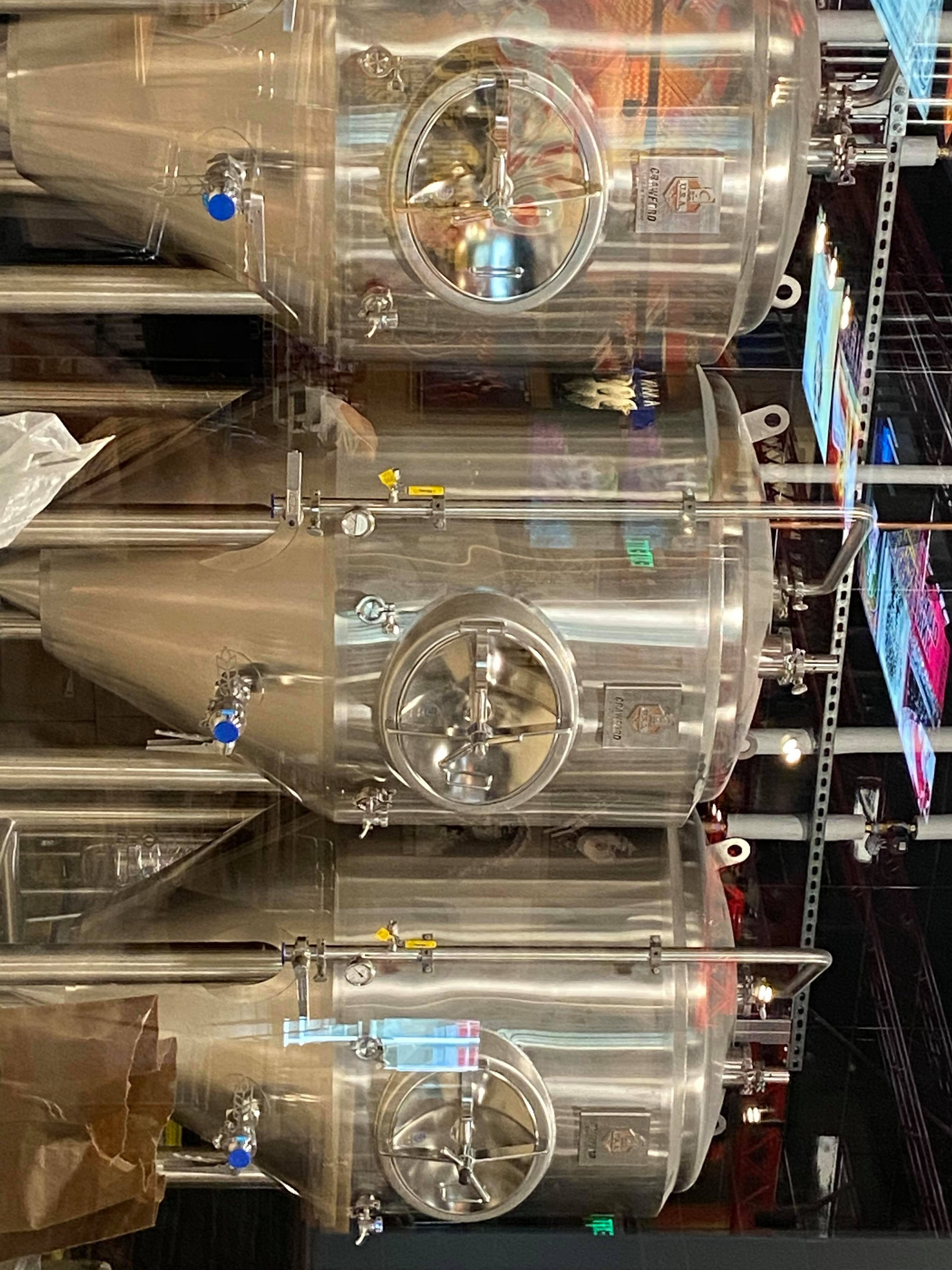 Stainless steel tanks with round doors, pipes, gauges, and valves, likely in a brewery or industrial setting.