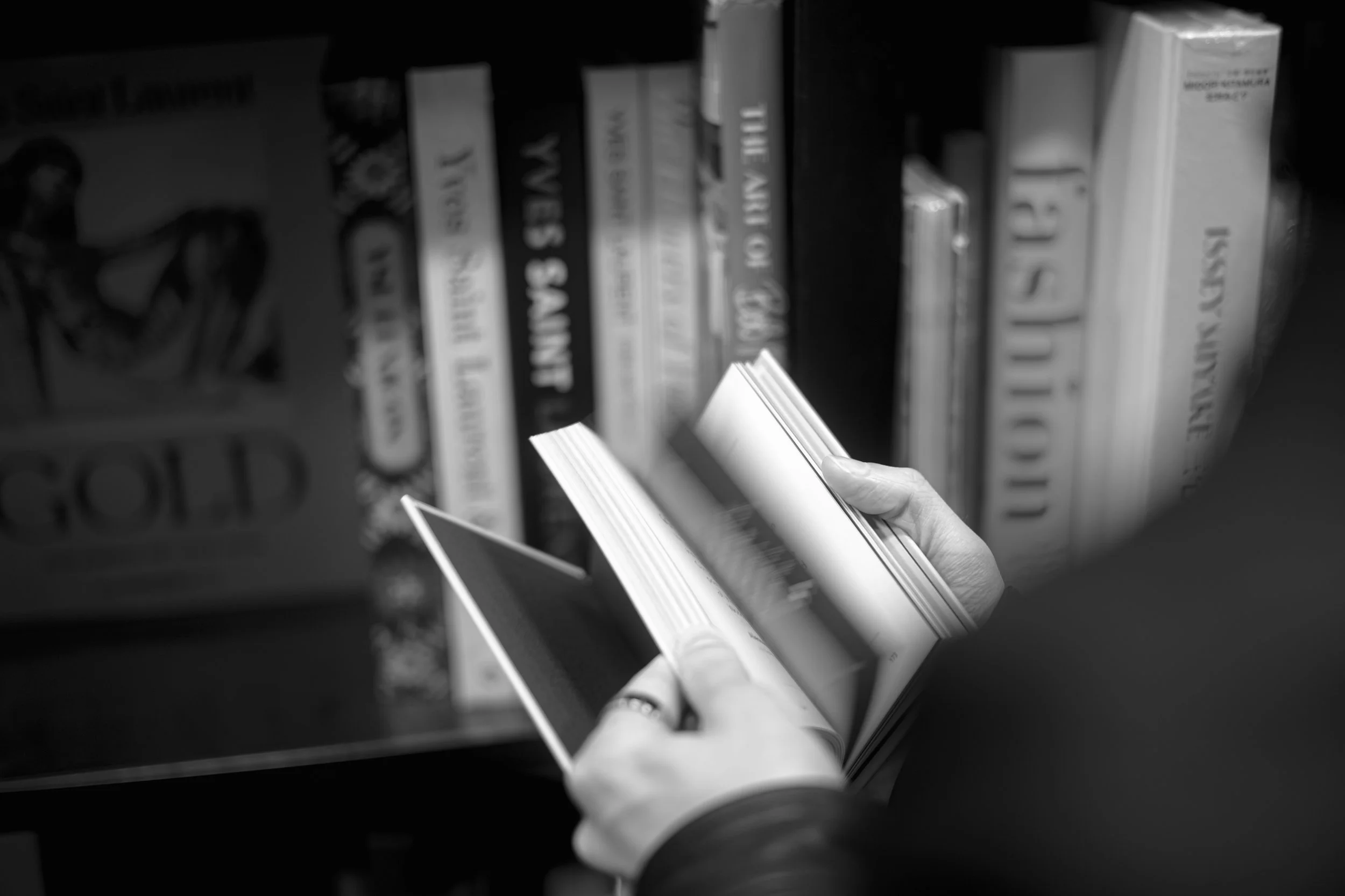 A person is holding and examining a book on a shelf in a bookstore, with other books lined up vertically in the background.