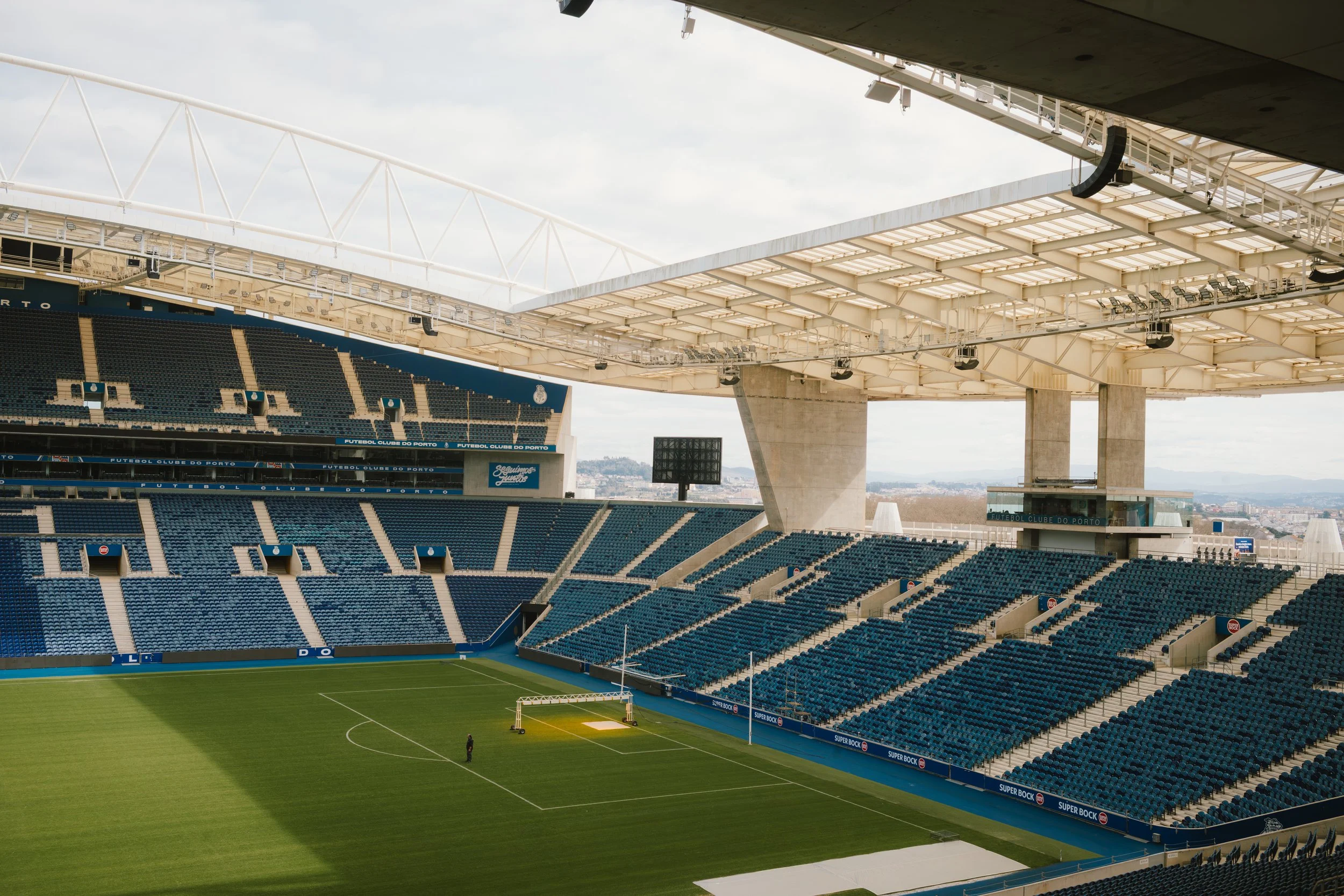 Empty soccer stadium with seating, field, and stadium roof overhead during daytime.
