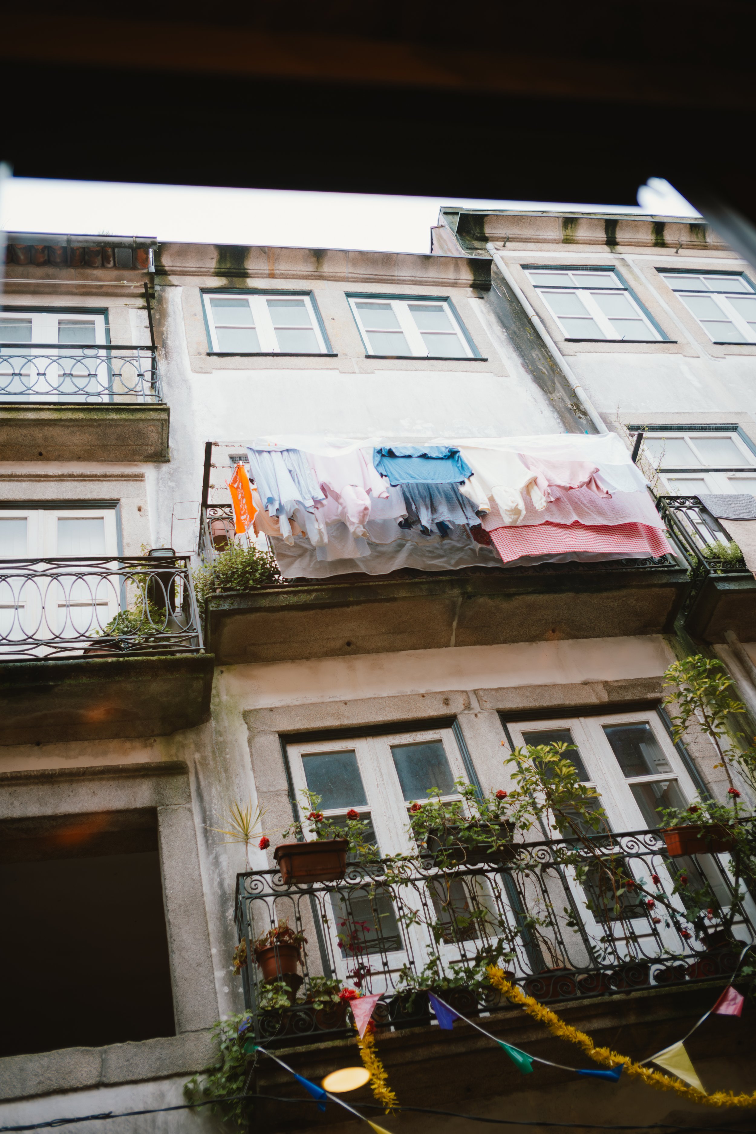 Four-story building with balconies decorated with potted plants, laundry hanging on a balcony, and colorful pennant banners strung across the lower part of the building.