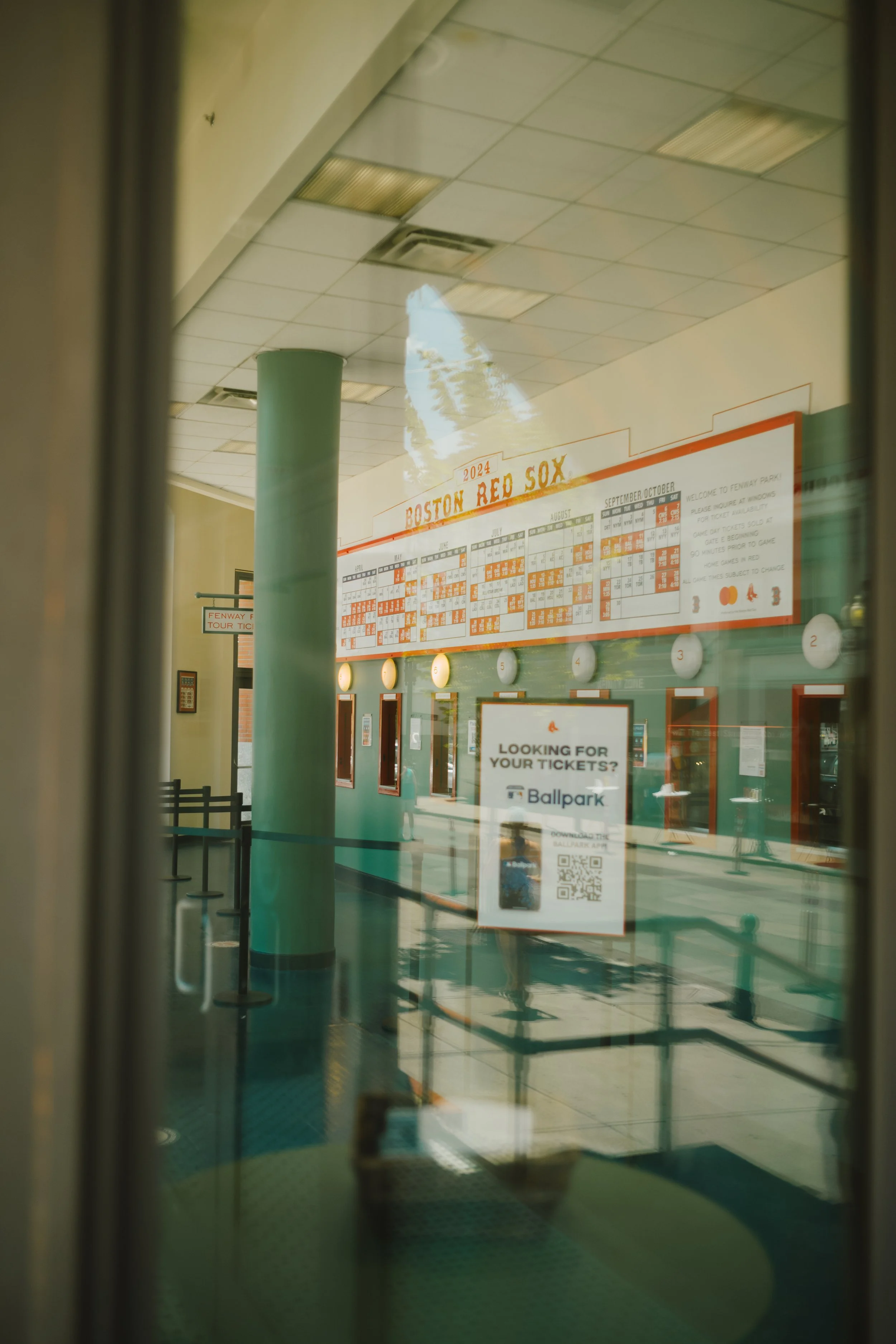View of a ticketing area at Fenway Park, home of the Boston Red Sox, with a large calendar for the 2024 baseball season on the wall and a sign encouraging visitors to download a ticket app.