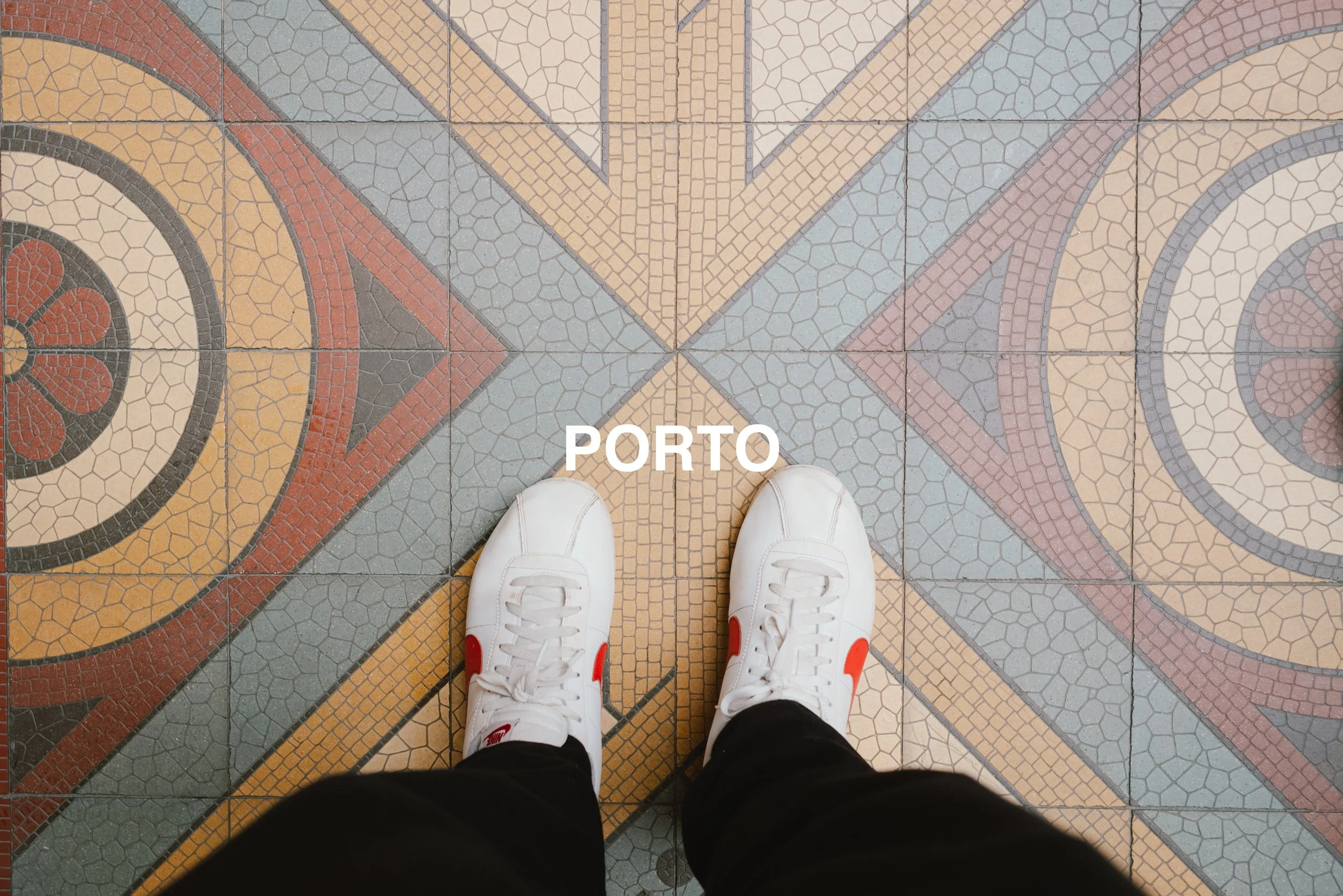 A person wearing white Nike sneakers standing on a colorful mosaic tile floor with the word 'PORTO' written on it.