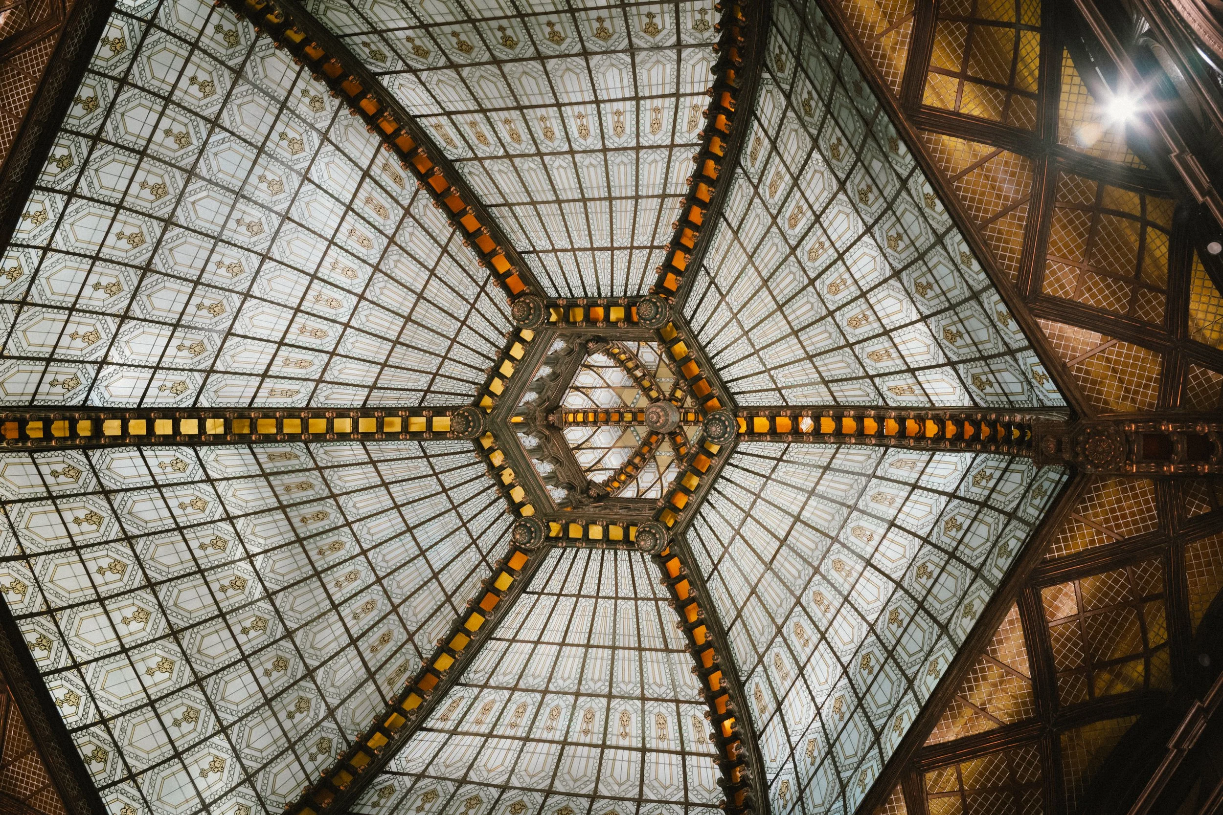 Interior view of an ornate glass and metal ceiling with decorative patterns and lighting fixtures.
