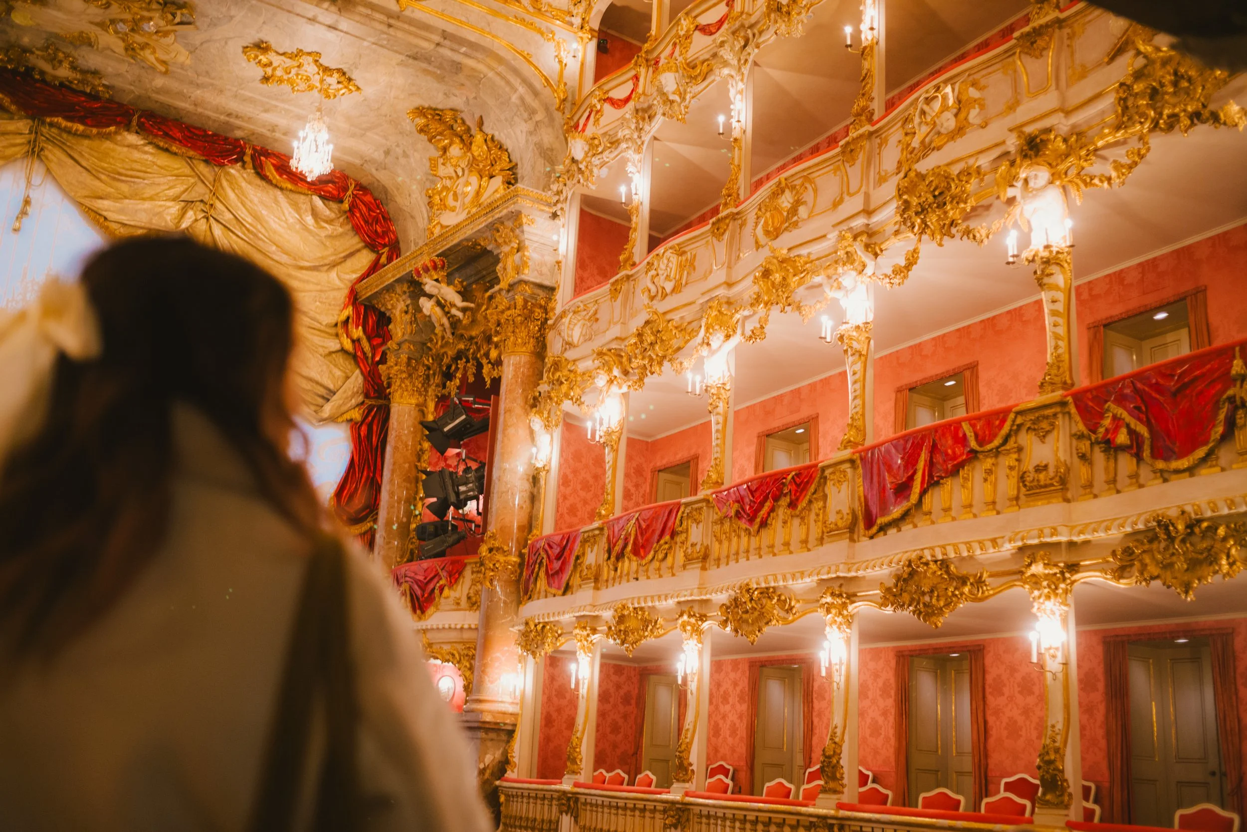 Interior of an ornate theater with gold embellishments, red drapes, and balconies, viewed from the audience.