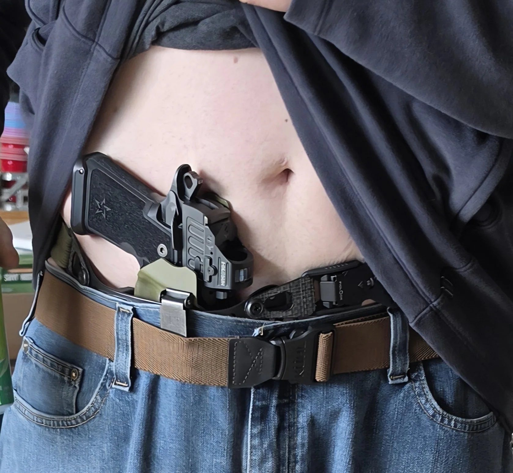 Close-up of a person wearing a tactical belt with a firearm holster, gun, and tactical gear, with part of their midriff and denim jeans visible.