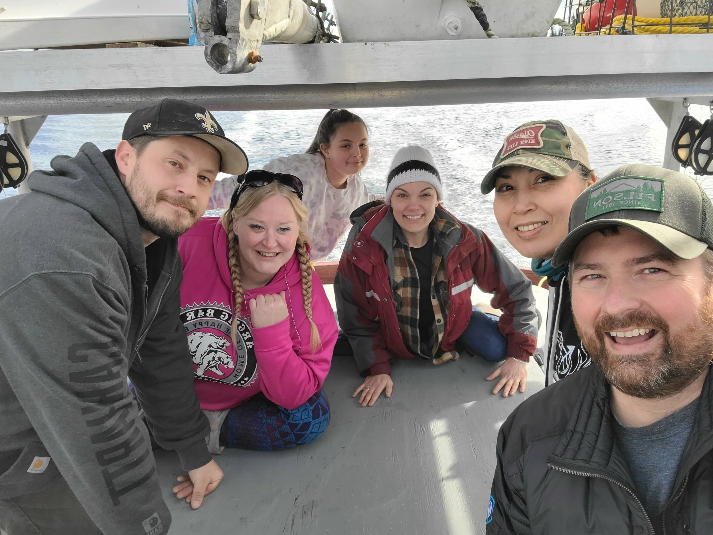 Group of six people on a boat, posing for a photo, with water in the background.