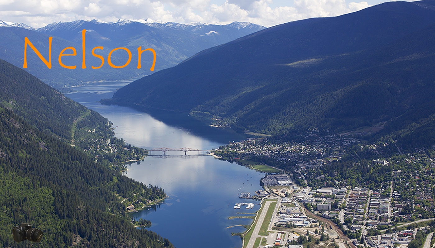Aerial view of Nelson, Oregon, showing a river running through a valley, surrounded by forested mountains, with a town and airport near the water.
