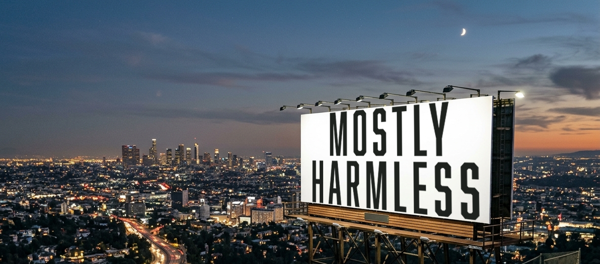 A city skyline at dusk with tall buildings and lights, featuring a billboard that reads 'Mostly Harmless' against a partly cloudy sky with a crescent moon.
