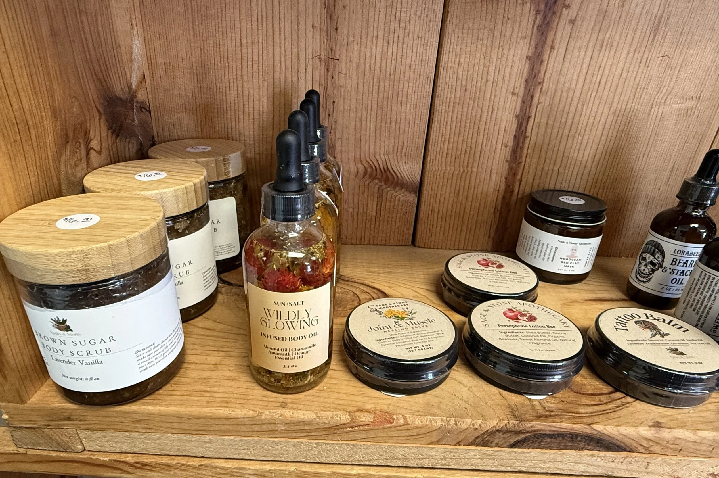 A wooden shelf holding various skincare and beauty products, including jars and bottles with labels such as body scrub, body oil, mask, and face cream.