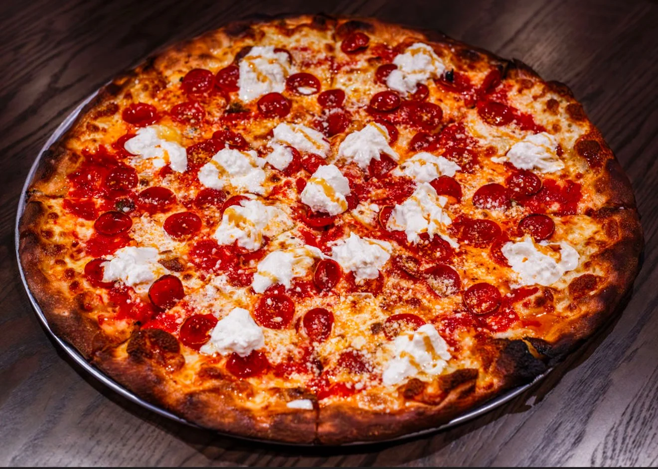 A pepperoni pizza with dollops of ricotta cheese on a wooden table.