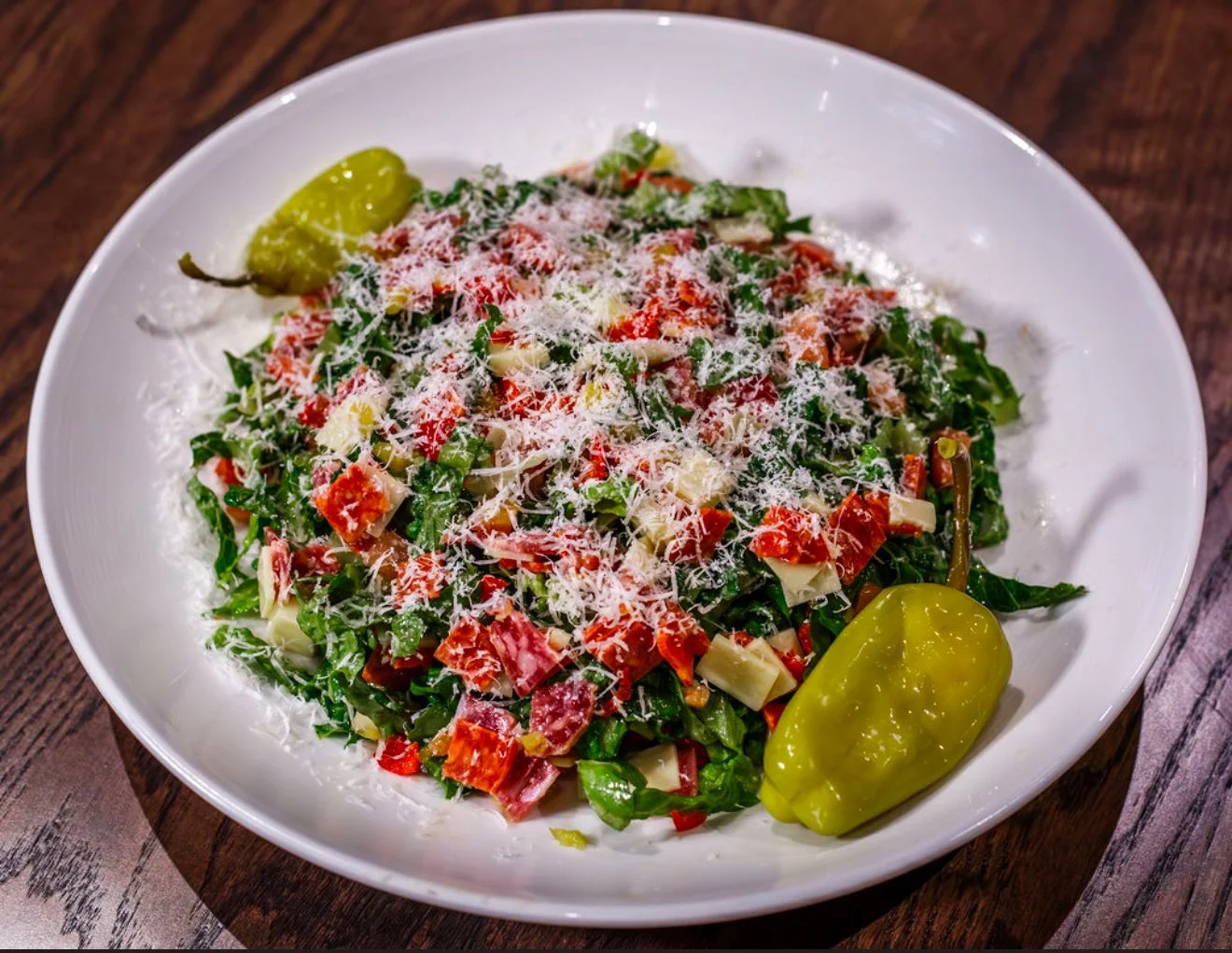 Fresh garden salad with chopped vegetables, shredded cheese, and two green chili peppers on a white plate.