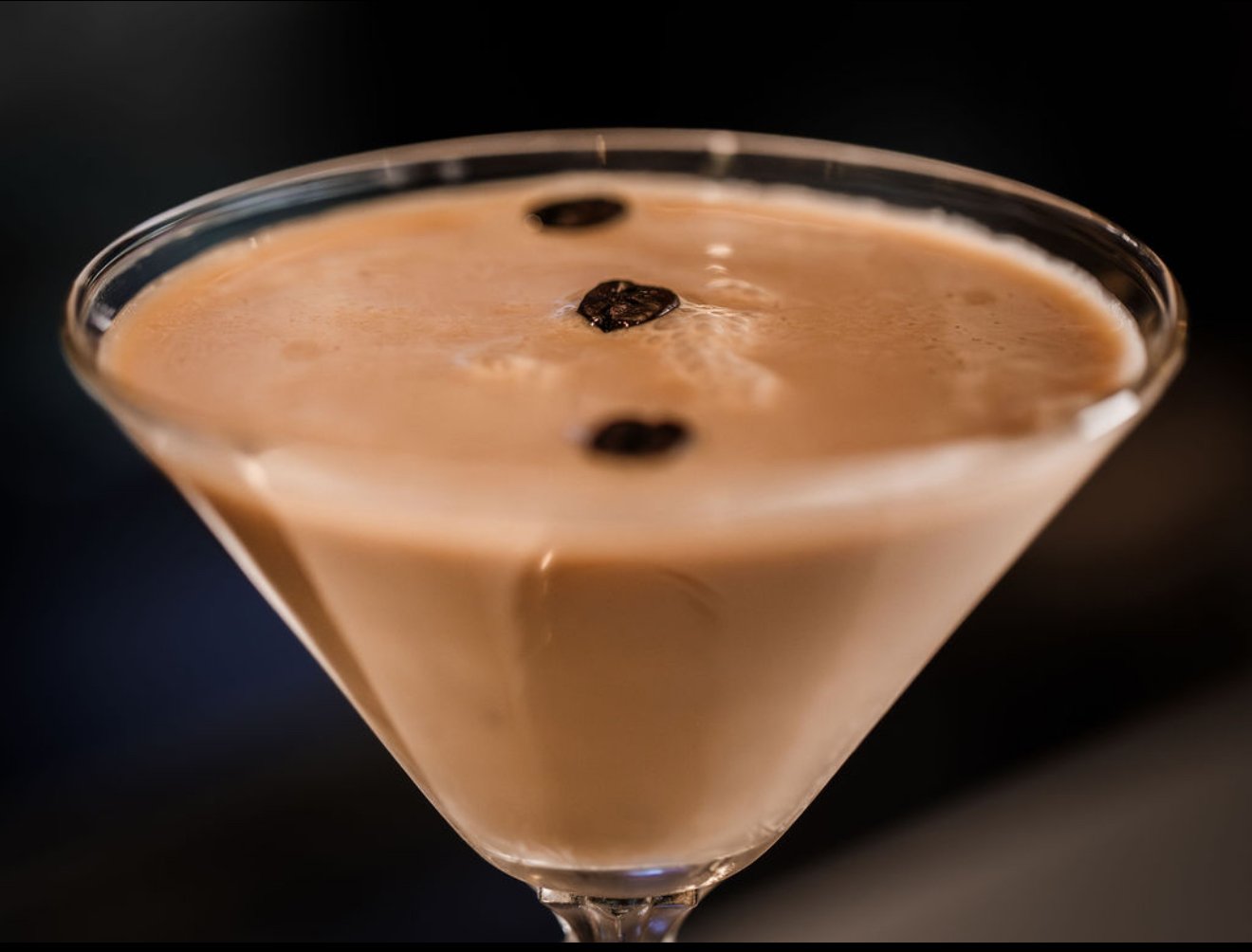 Close-up of a creamy coffee cocktail garnished with three dark coffee beans in a martini glass.