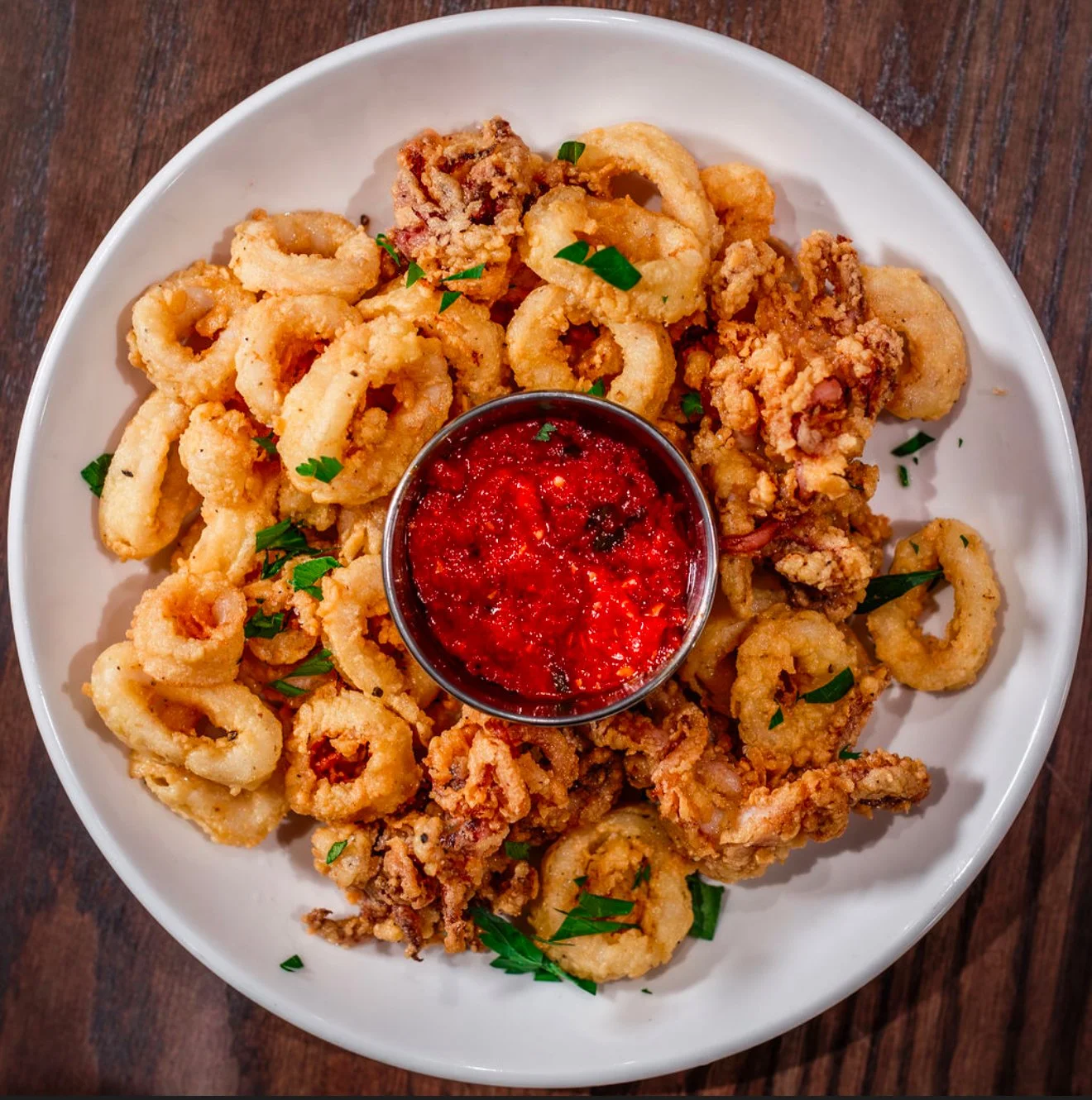 Fried calamari with a side of red dipping sauce on a white plate.