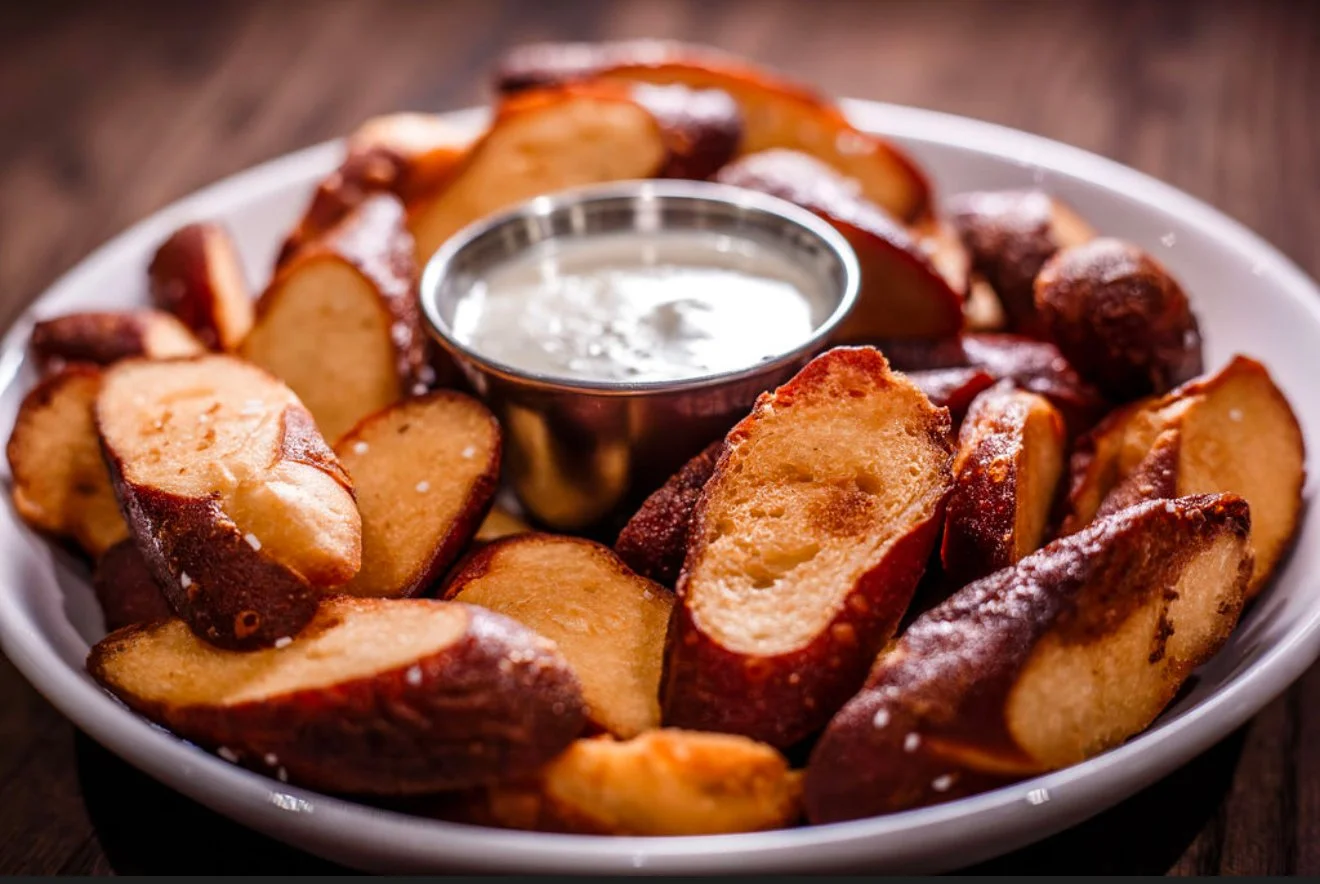 Plate of golden-brown potato wedges with a small bowl of creamy dipping sauce in the center.