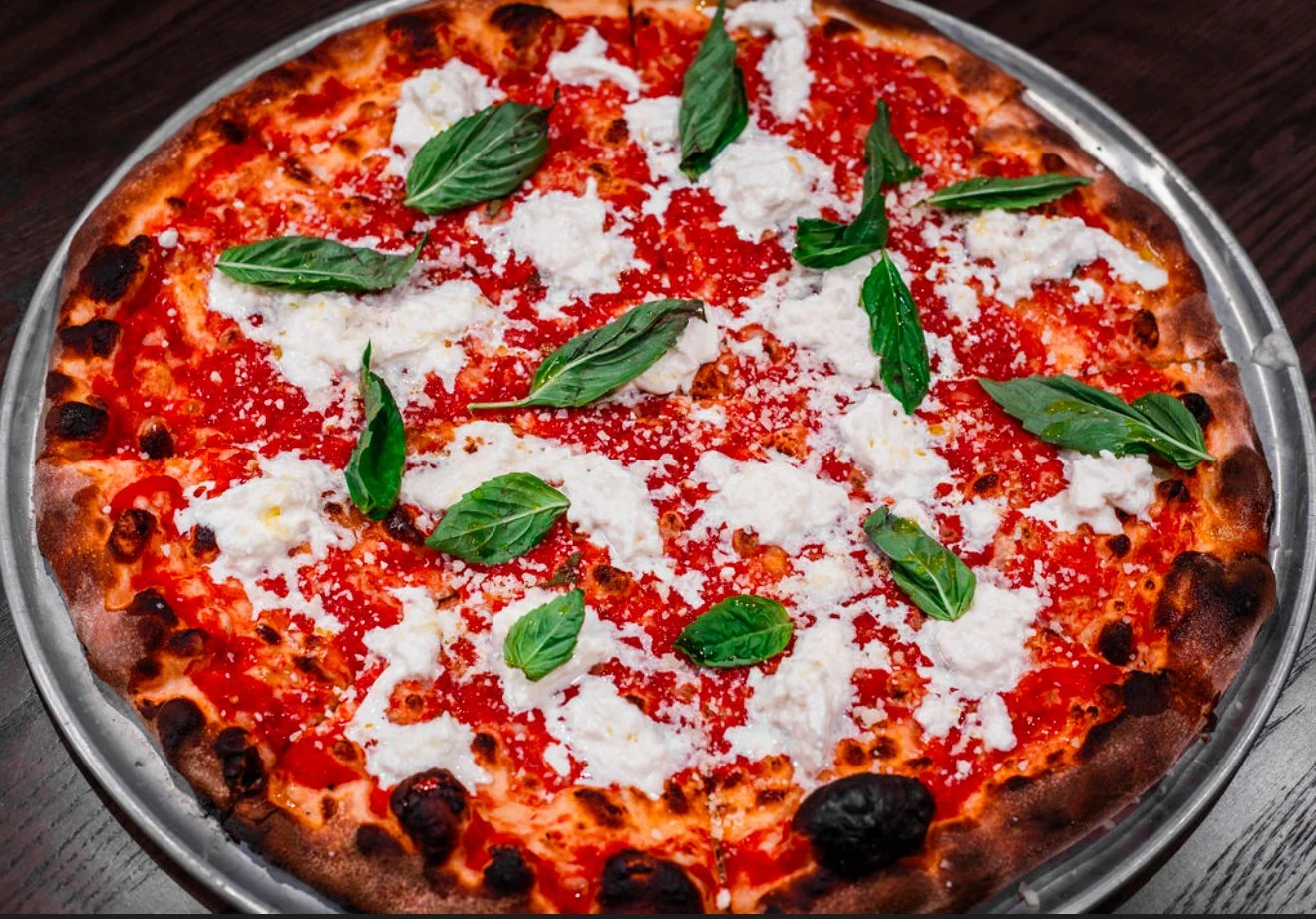 A pizza topped with tomato sauce, chunks of white cheese, fresh basil leaves, and sprinkled with grated cheese on a metal tray