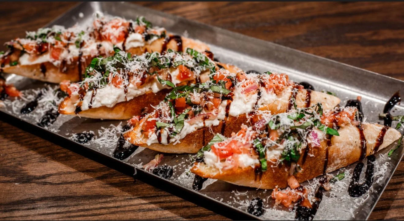 Three pizza slices topped with tomatoes, basil, cheese, and drizzled with balsamic glaze, served on a rectangular metal tray.