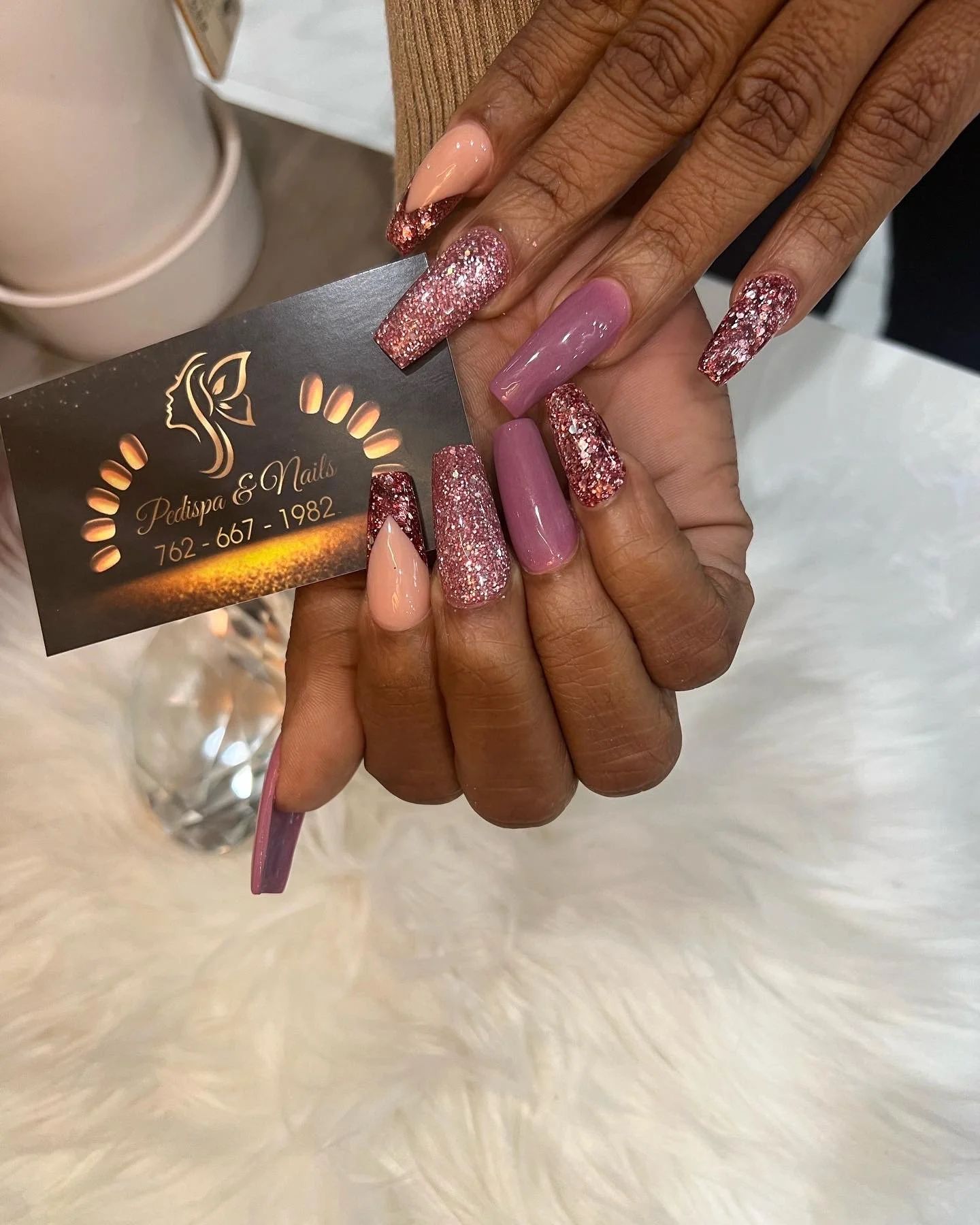 Close-up of well-manicured hands with pink and glittery nails holding a business card for Pedispa & Nails.
