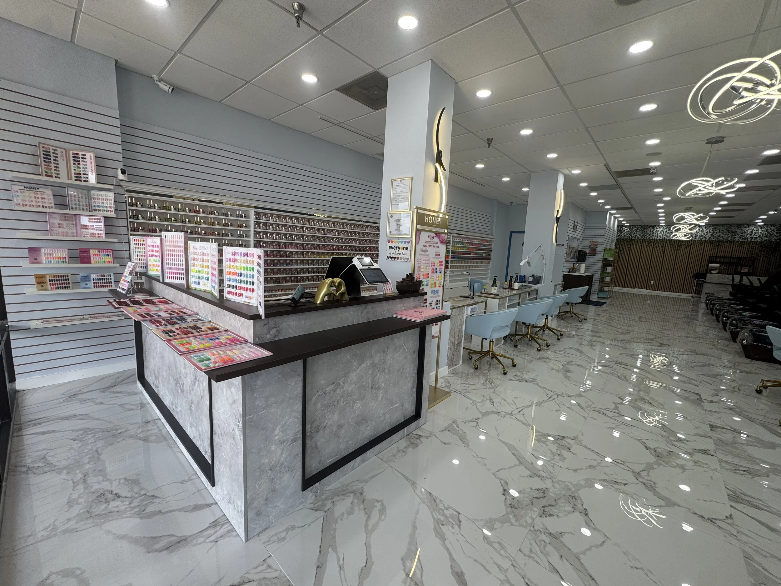 Interior of a nail salon with a display of nail polish colors, a reception desk, seating area, and decorative lighting on the ceiling.