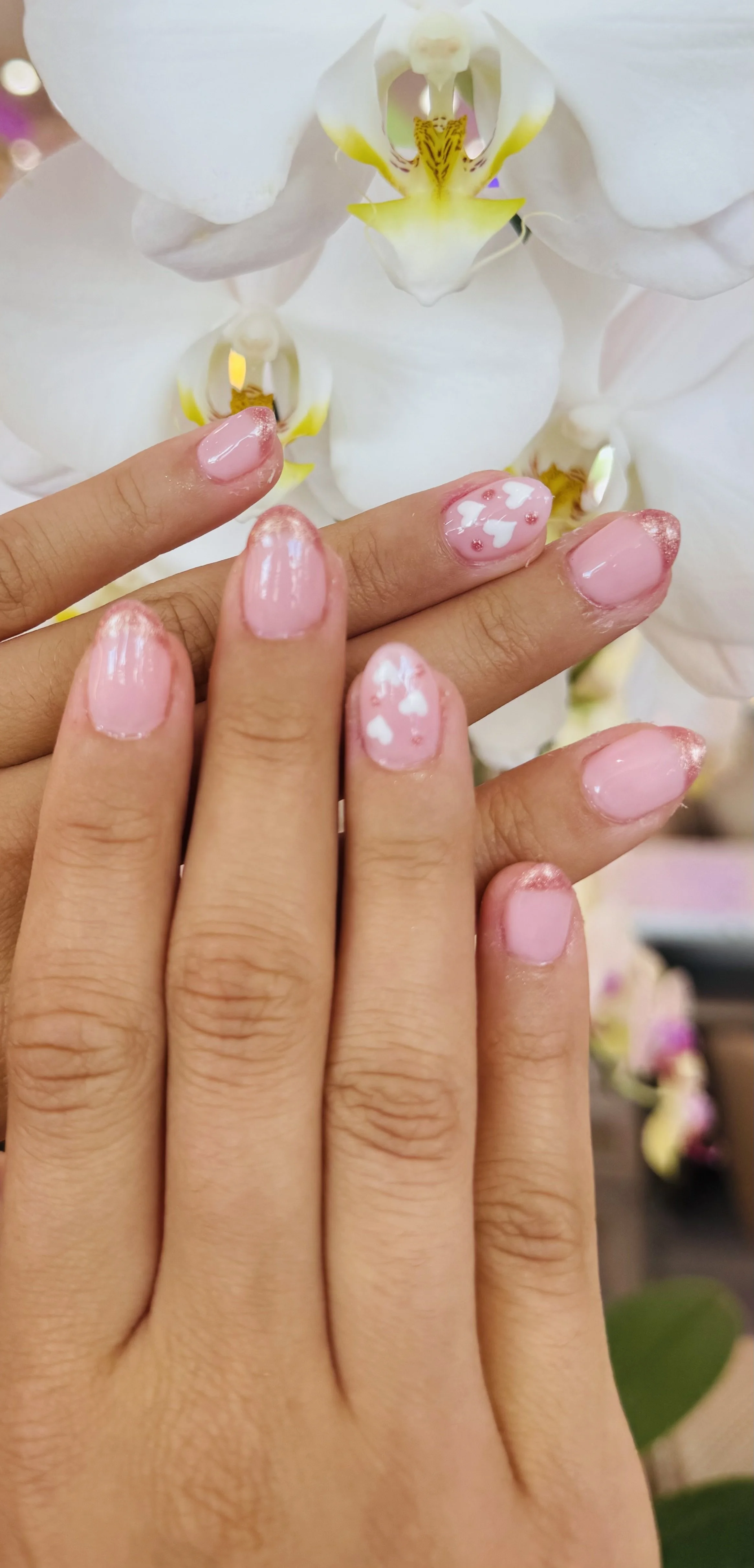 Close-up of a person's hand with decorated nails in front of white orchid flowers.