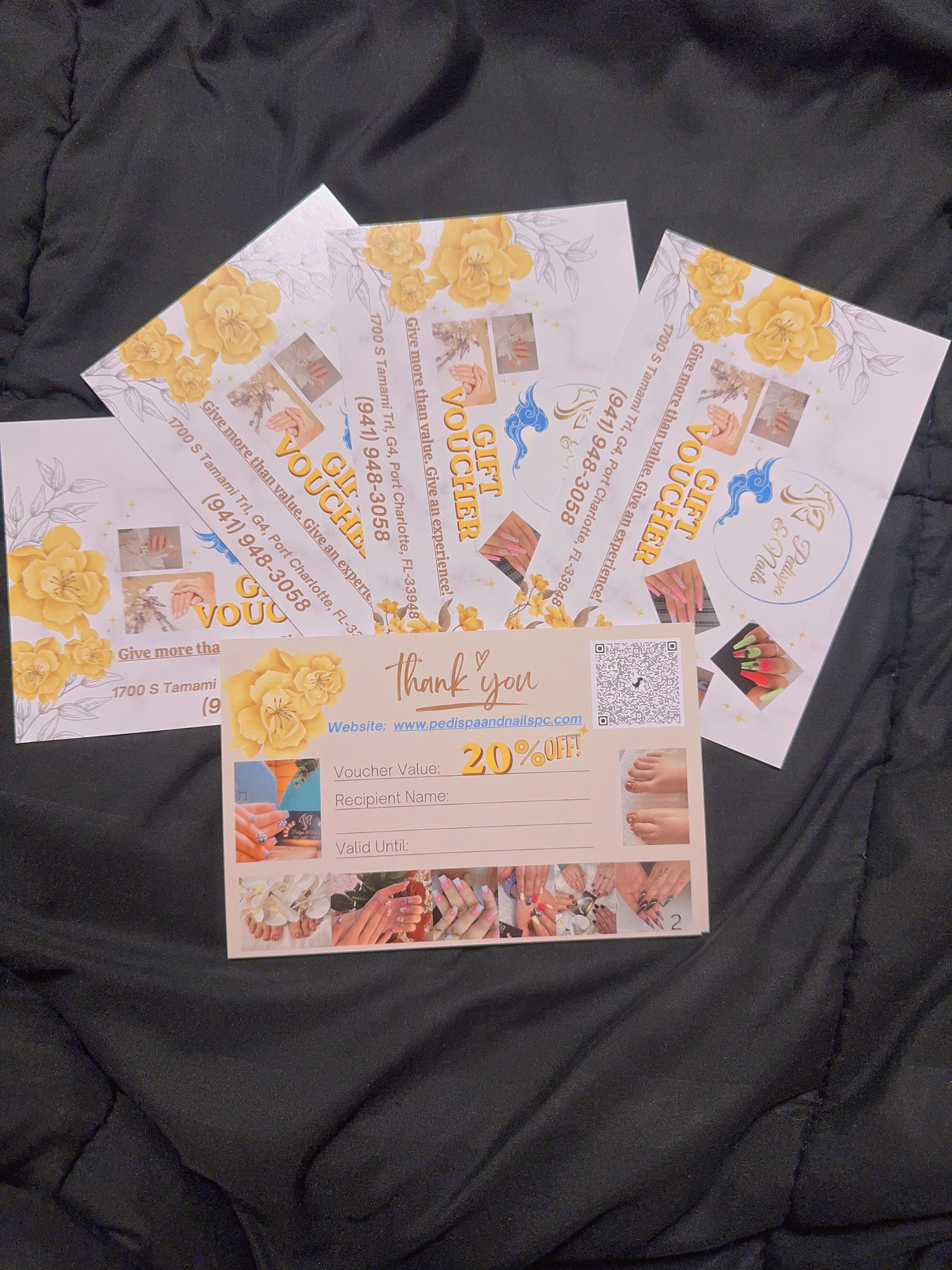 Multiple nails salon gift vouchers with yellow floral design, images of nails being painted, and a QR code, placed on a black leather surface.