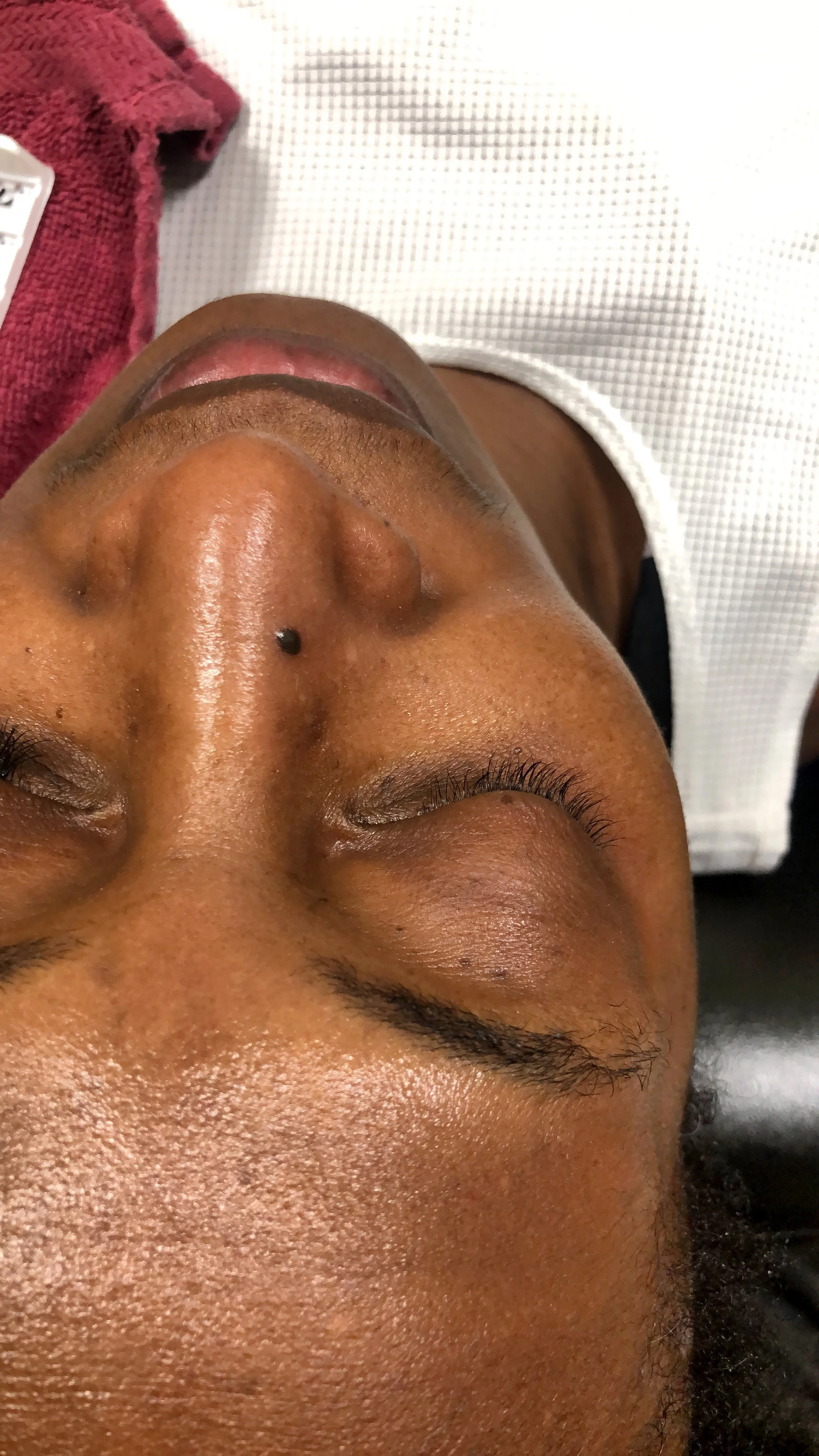 Close-up of a person's face with closed eyes, lying down, with a towel nearby.