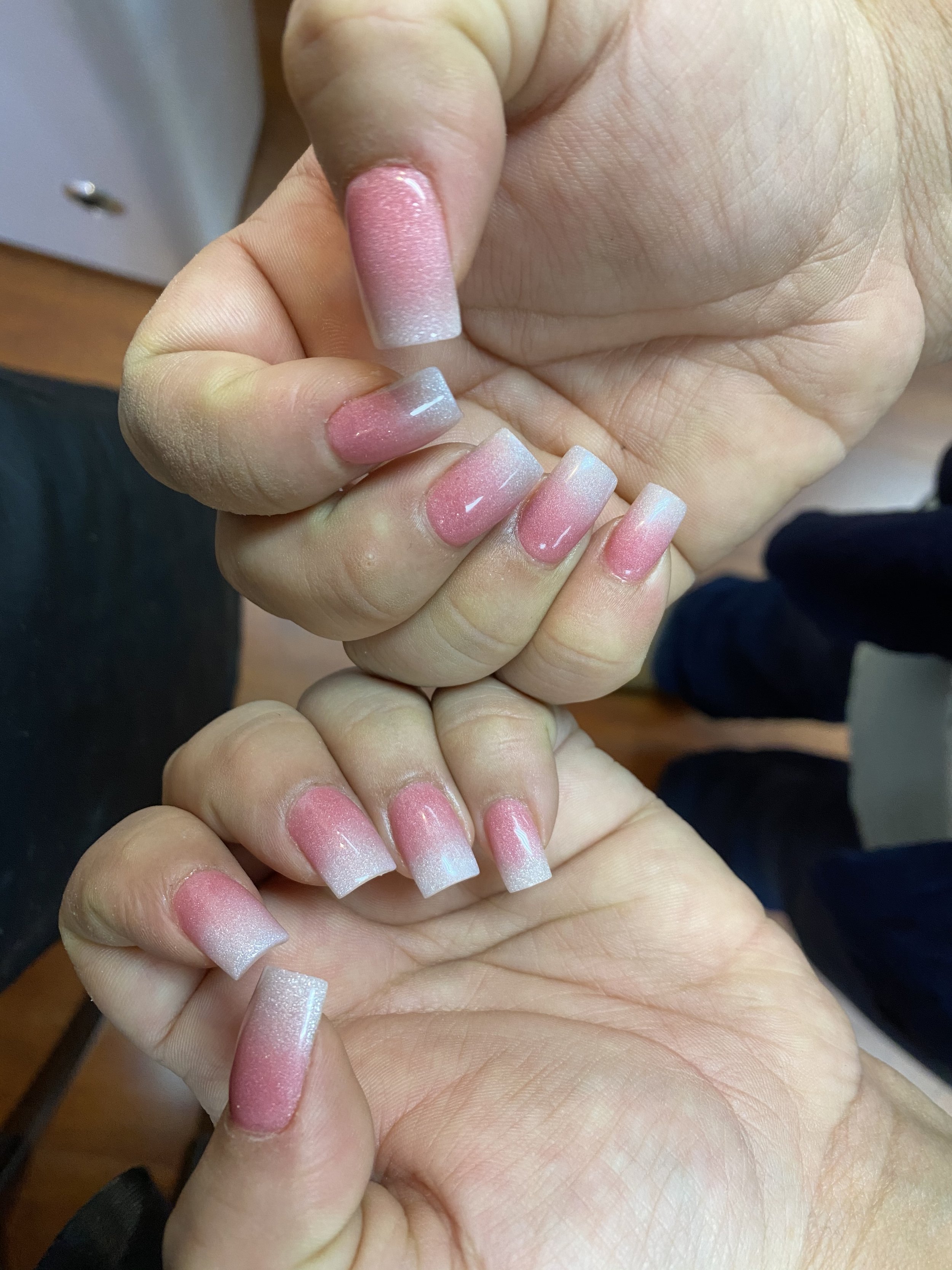 Close-up of a person's hand with pink and white ombre acrylic nails, held in a position to showcase the nails.