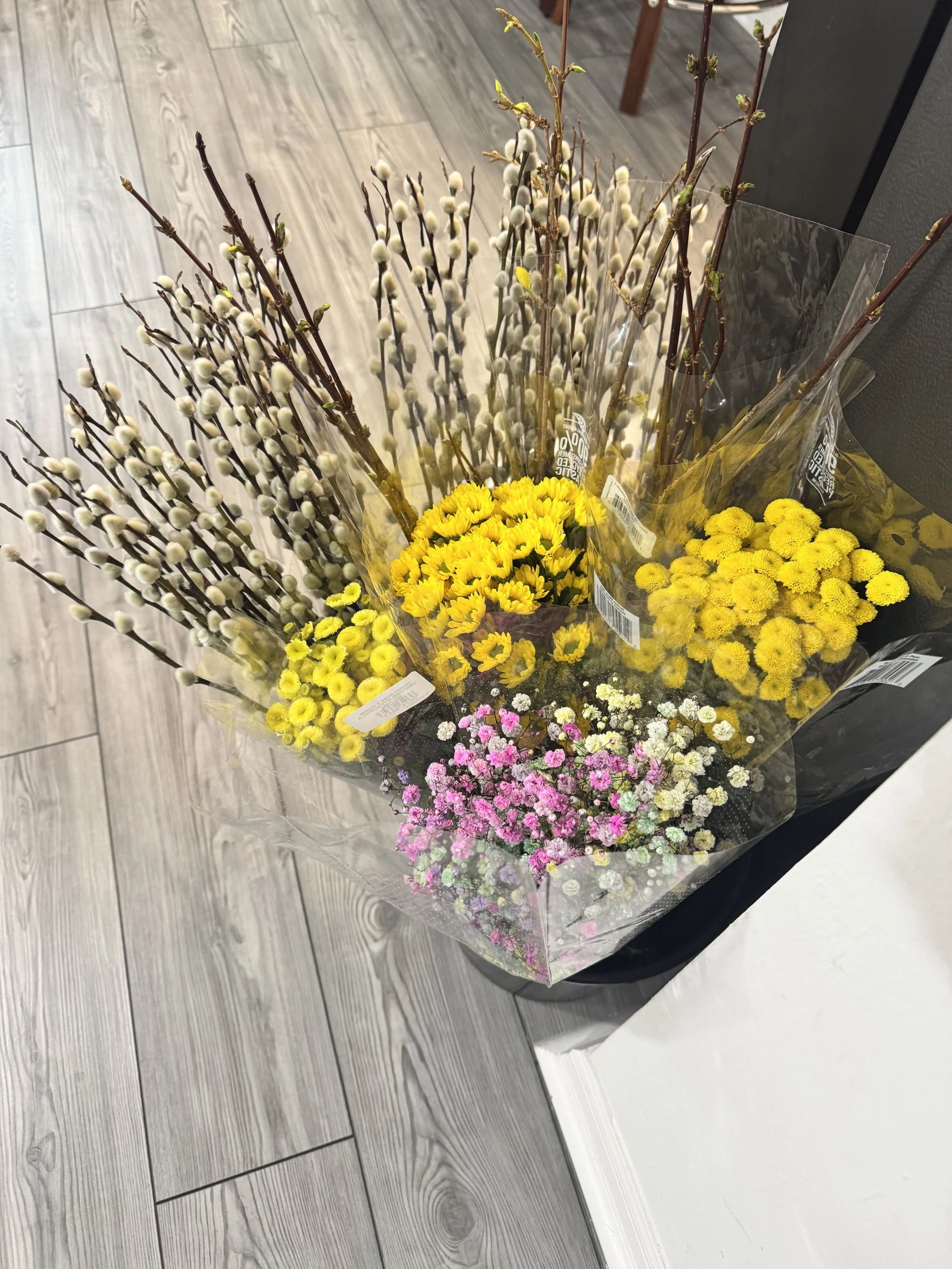 Bouquet of yellow, pink, and white flowers wrapped in clear plastic on a gray wood floor.