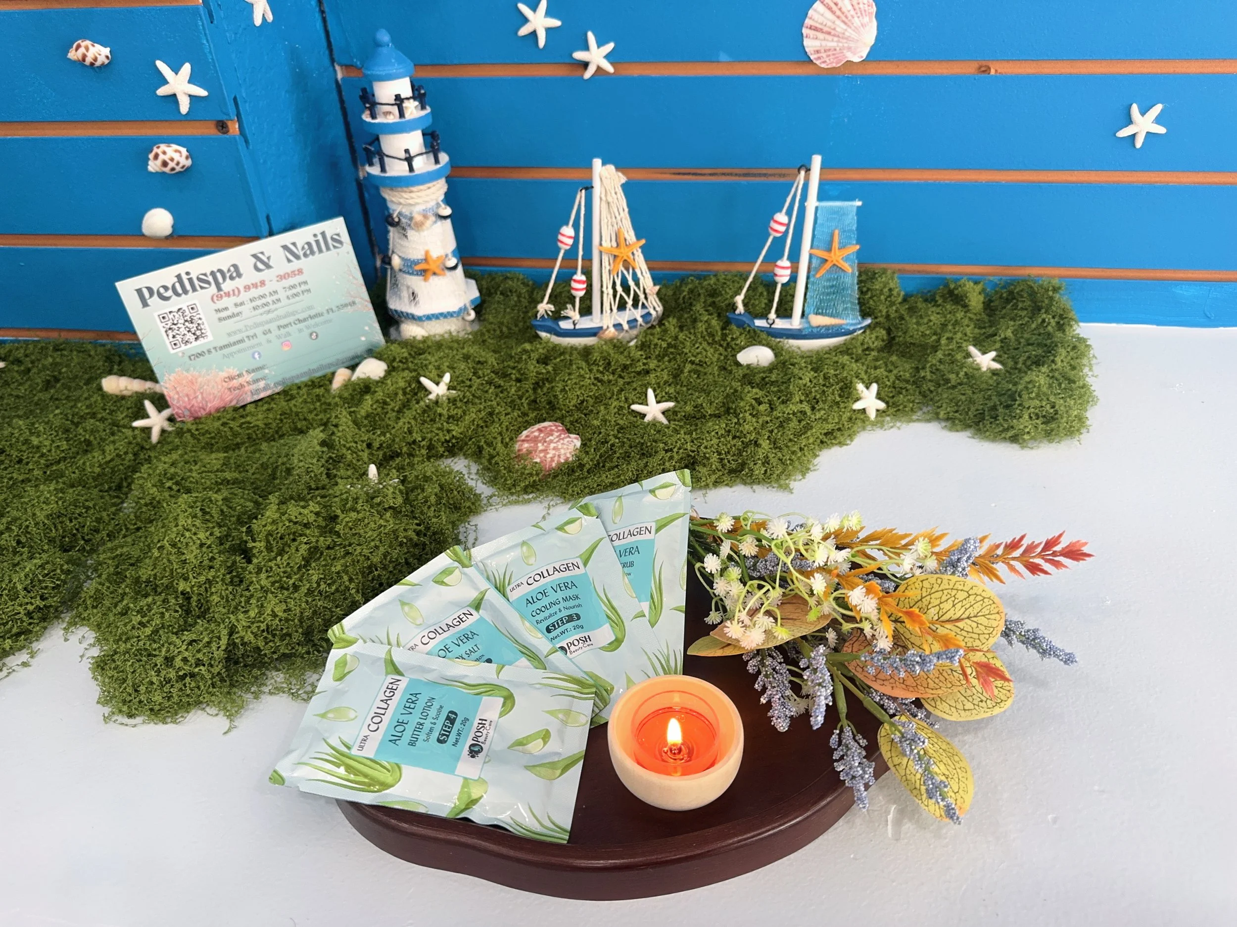 A display with nautical-themed decorations, including a lighthouse, miniature sailboats, shells, starfish, greenery, and a lit candle.