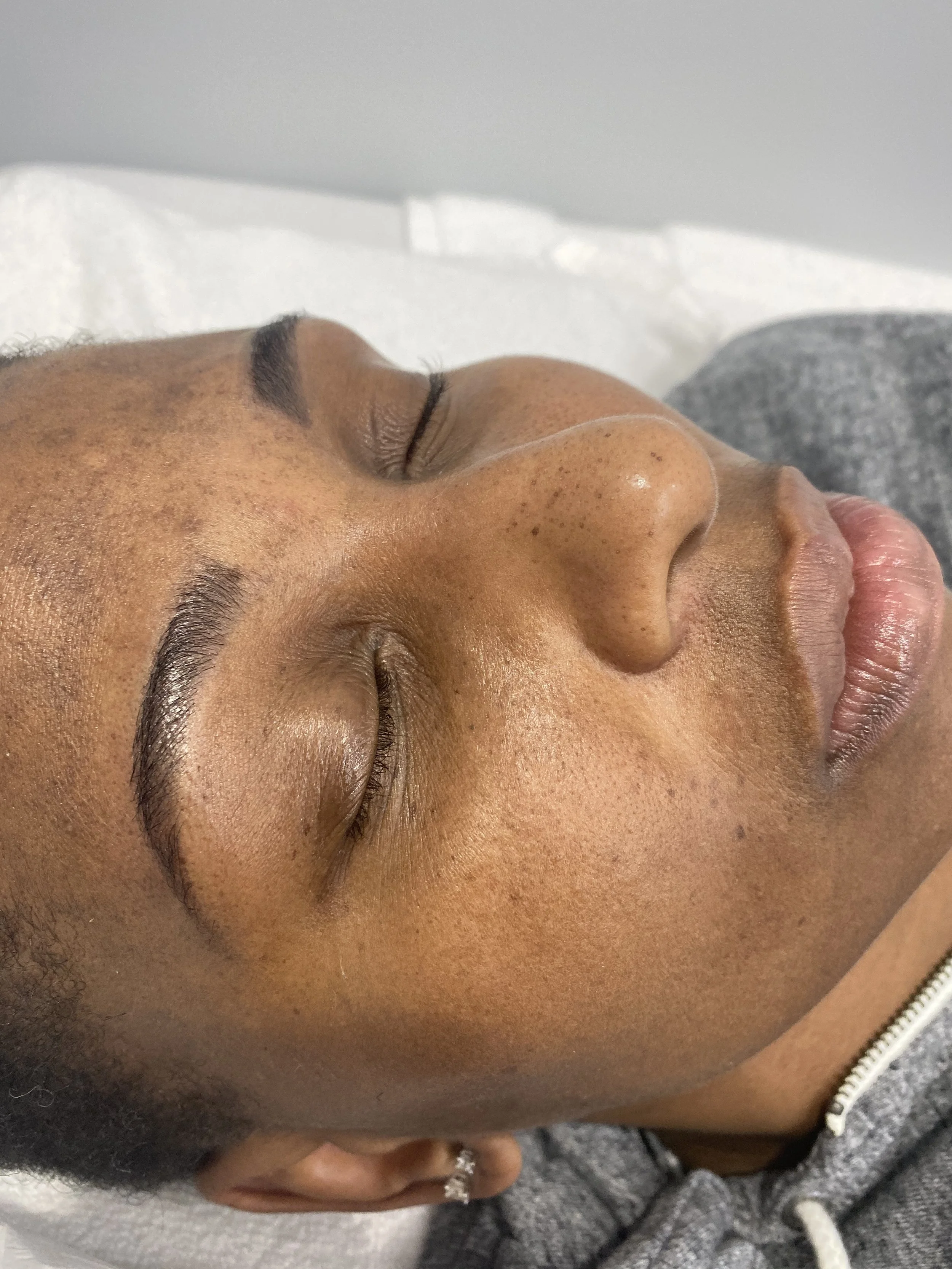 Close-up of a person with brown skin and closed eyes, resting, showing facial features, eyebrows, and part of the nose and lips.