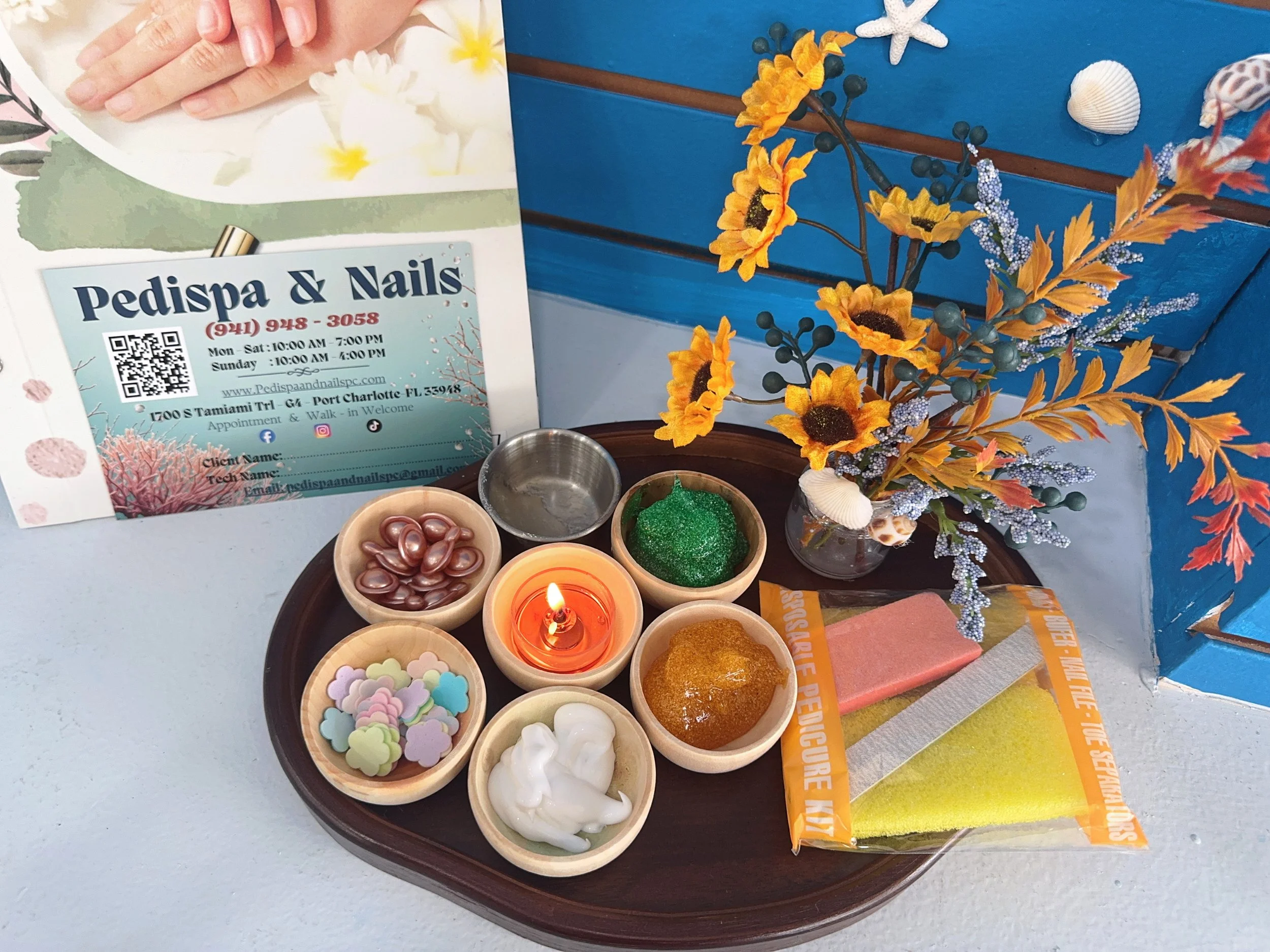 Decorative table display with small bowls of colorful candies, glue, and decorations, alongside a bouquet of yellow and orange flowers, with promotional flyers and a blue background.