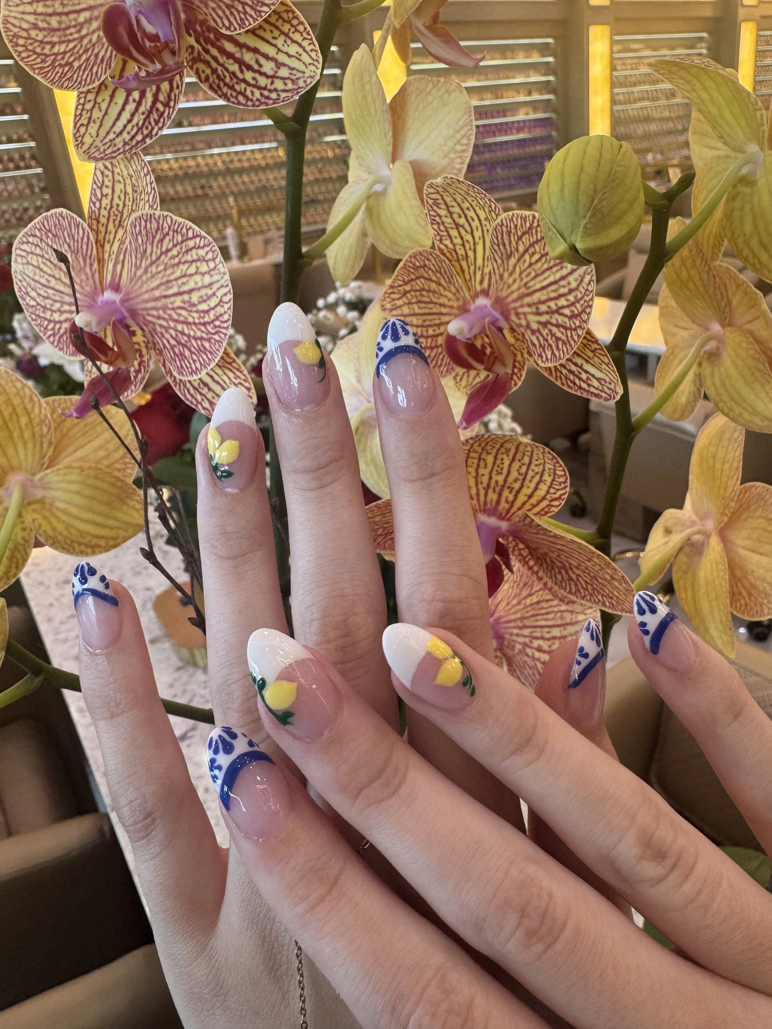 A person's hand with decorated fingernails resting on a bunch of yellow orchids with red and purple veining.