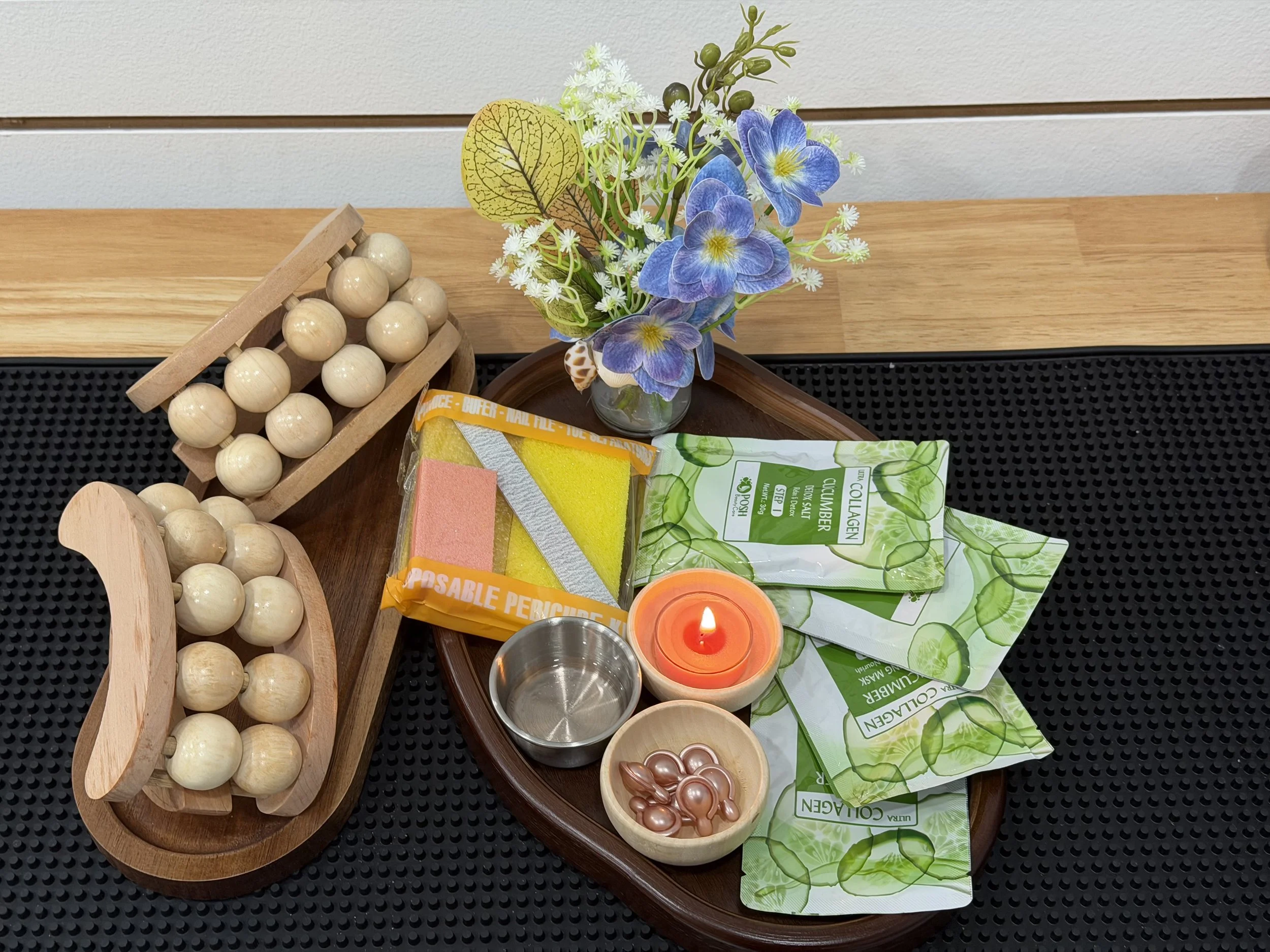 A flower arrangement with purple and white flowers, green leaves, and a candle, along with various bath and beauty products on a wooden table.