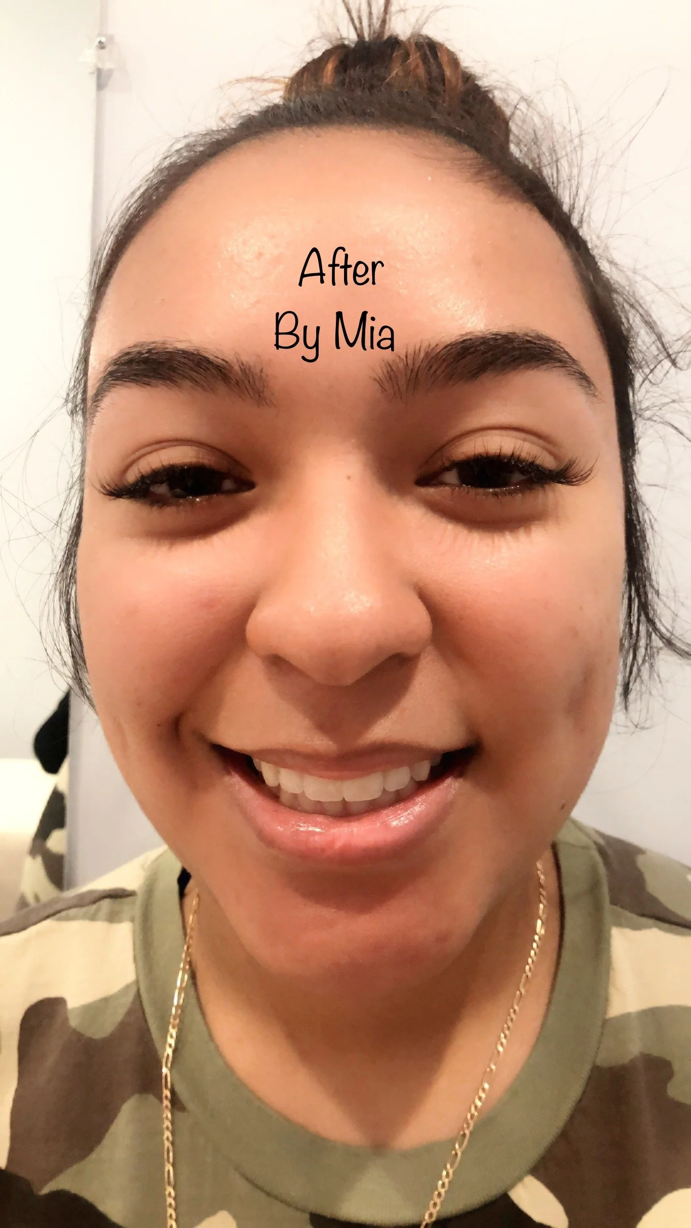 A woman smiling with her eyes partially closed, wearing makeup with long eyelashes, a camouflage shirt, and a gold chain necklace. Text overlay reads 'After By Mia.'