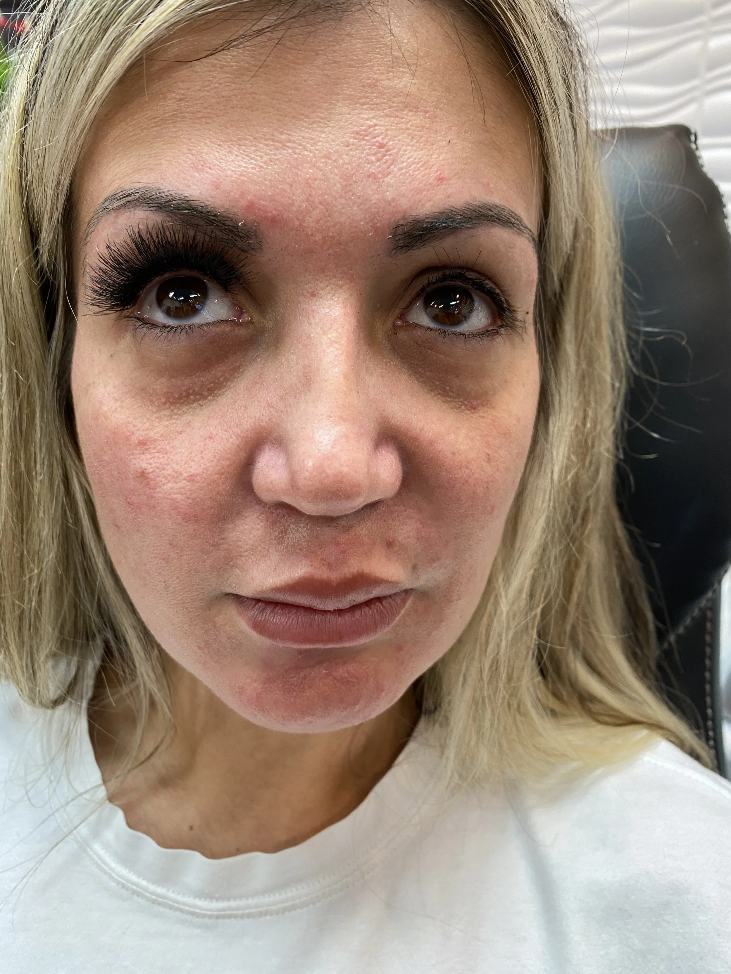 Close-up of a woman's face with makeup and natural skin texture, wearing a white top.