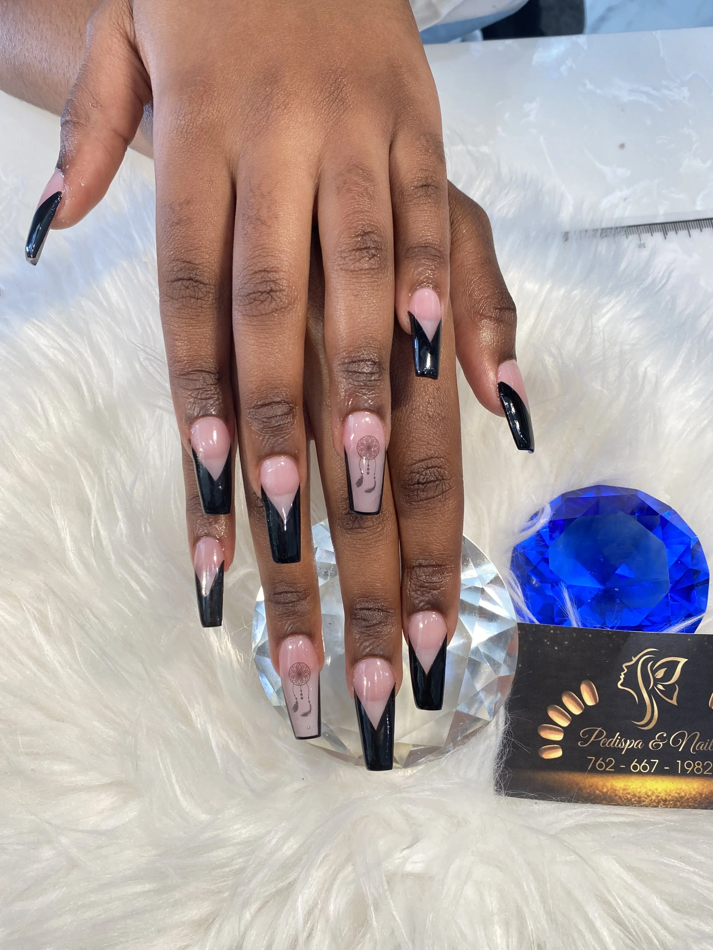 Close-up of a hand with long black and pink nails resting on a soft white fur surface, with a business card partially visible nearby.