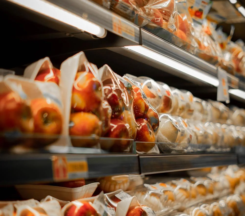 Shelves in a grocery store display pre-packaged apples in plastic containers.