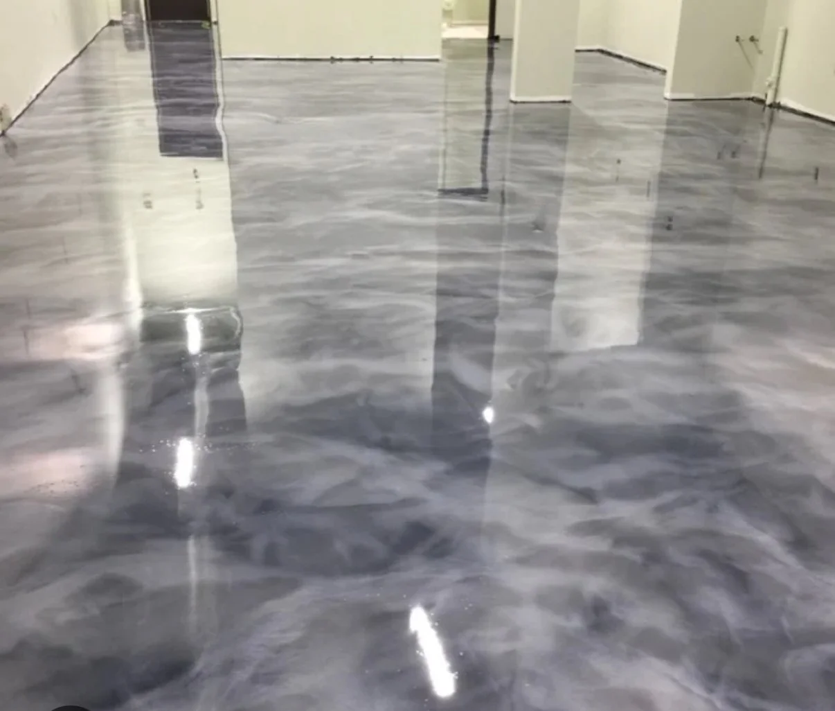 The image shows a room with a polished, shiny, gray marbled floor. The floor reflects the surrounding walls and some light fixtures. The room appears to be under construction or renovation, with unfinished walls and visible piping.