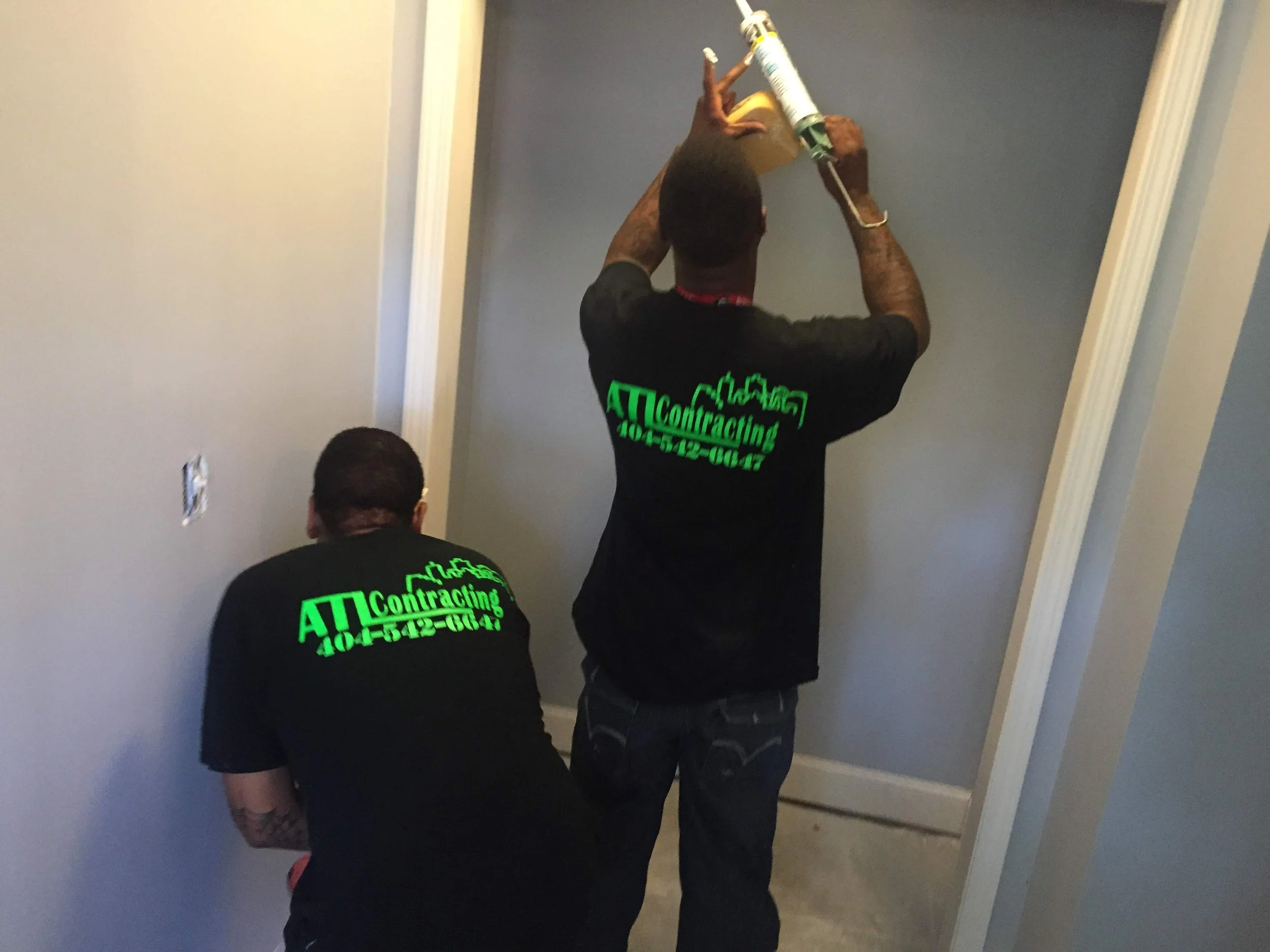 Two men working on a construction project, from ATL Basement Solutions.com  with one holding a caulking gun and the other painting in a basement in Union City Ga.